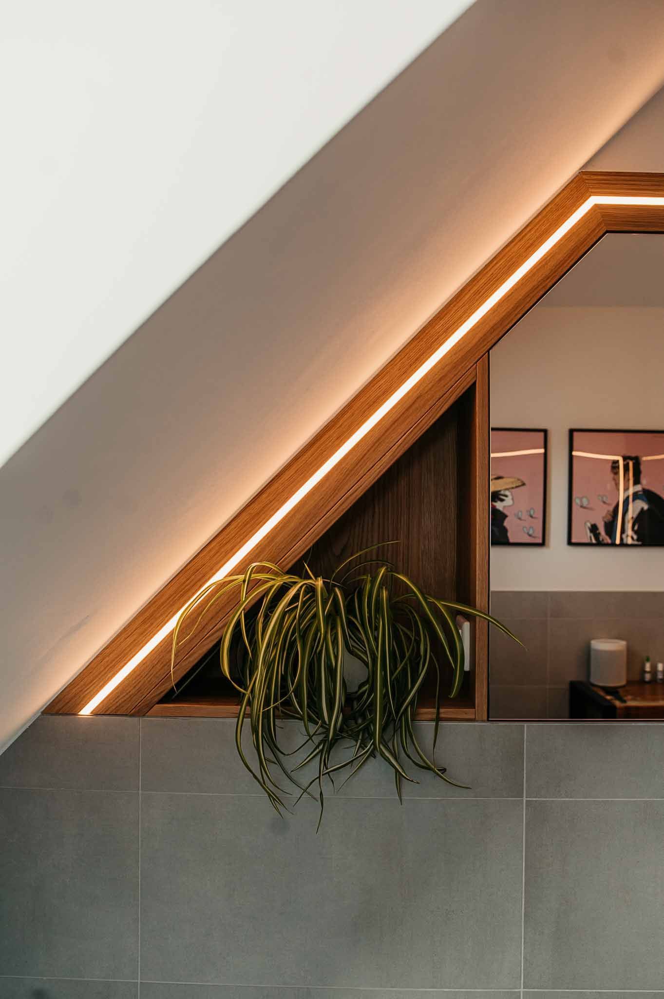 Ein kleines Fenster mit einer Hängepflanze, umrahmt von Holz und warmer Beleuchtung, in einem Raum mit Kunst.