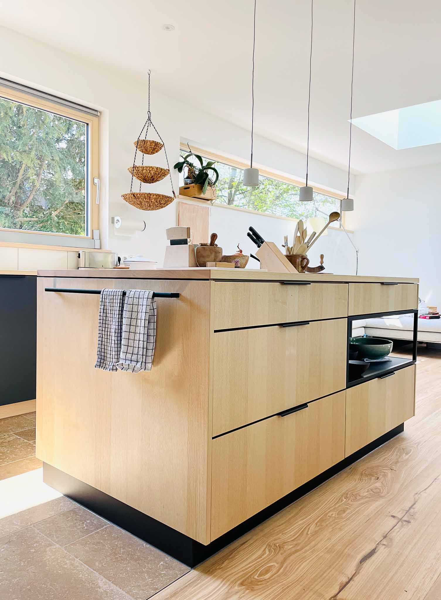 Moderne Küche mit einer hellen Holzinsel, dunklen Akzenten und Hängelampen.