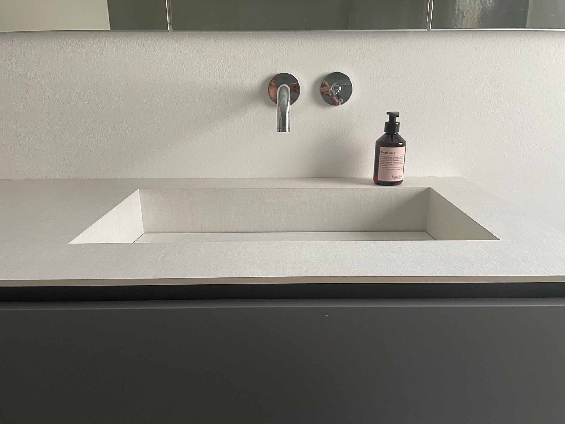 Modernes Badezimmerwaschbecken mit eingebautem Becken, silbernem Wasserhahn und dunkelgrauem Schrank. Beige Arbeitsplatte mit Seifenspender.