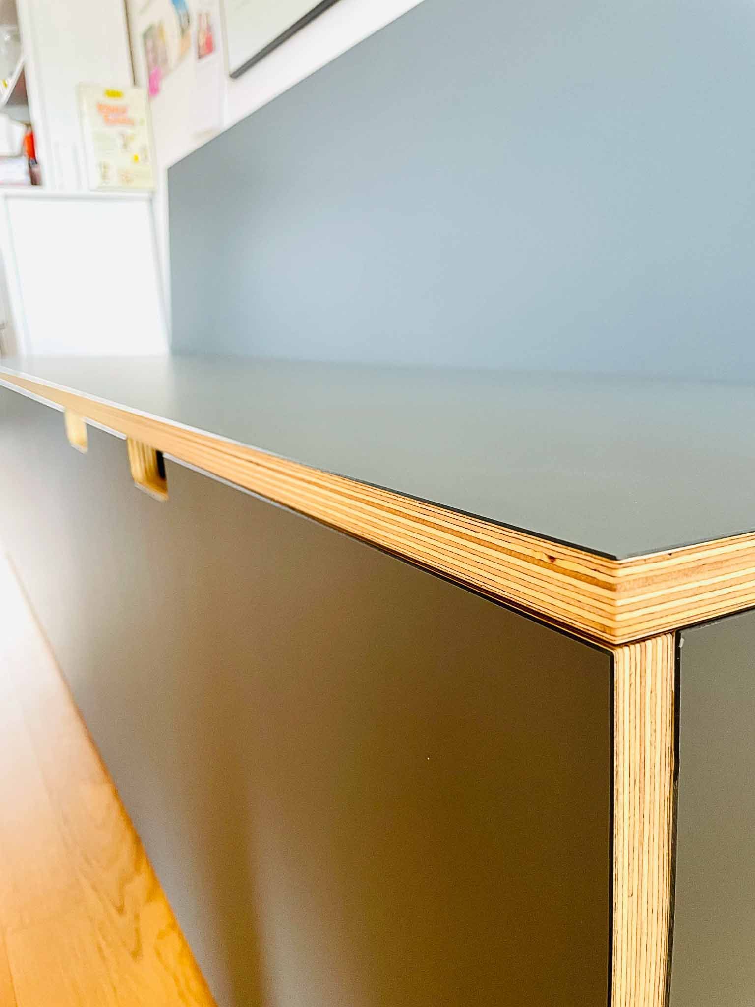 Nahaufnahme eines grauen Schranks mit freiliegenden Holzkanten vor einer blauen Wand und einem Holzboden.