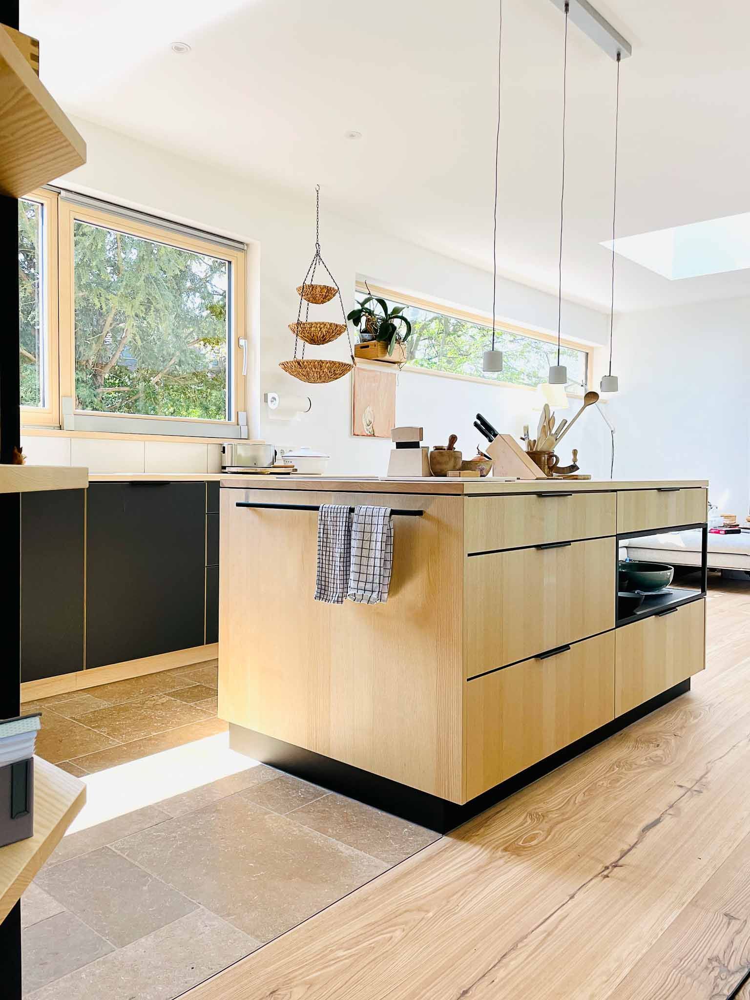 Moderne Küche mit Holzinsel, Schränken und einer Hängepflanze. Helles Tageslicht.