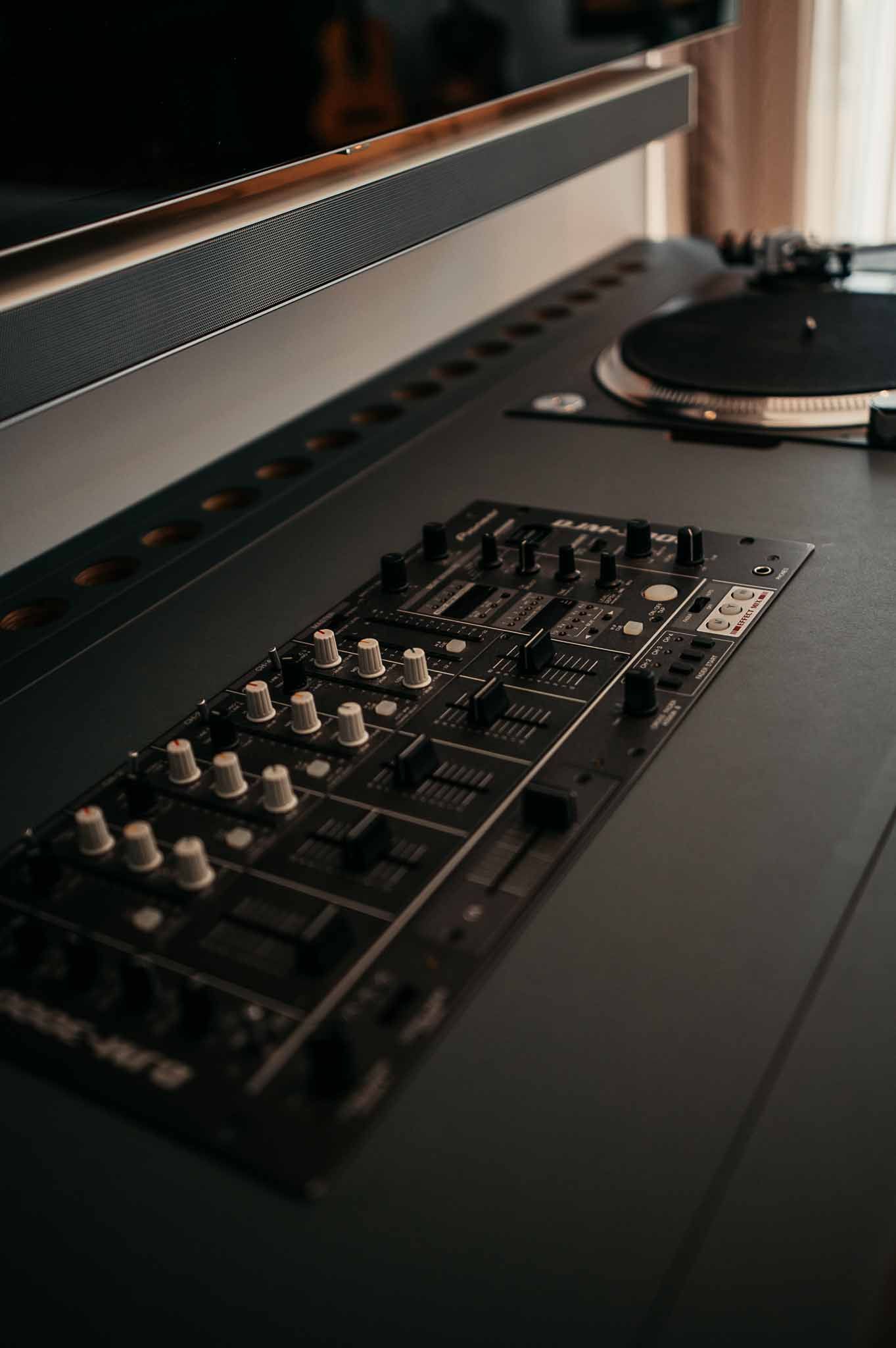 DJ-Mixer und Plattenspieler-Setup, schwarz mit weißen Knöpfen, in einem schwach beleuchteten Raum.