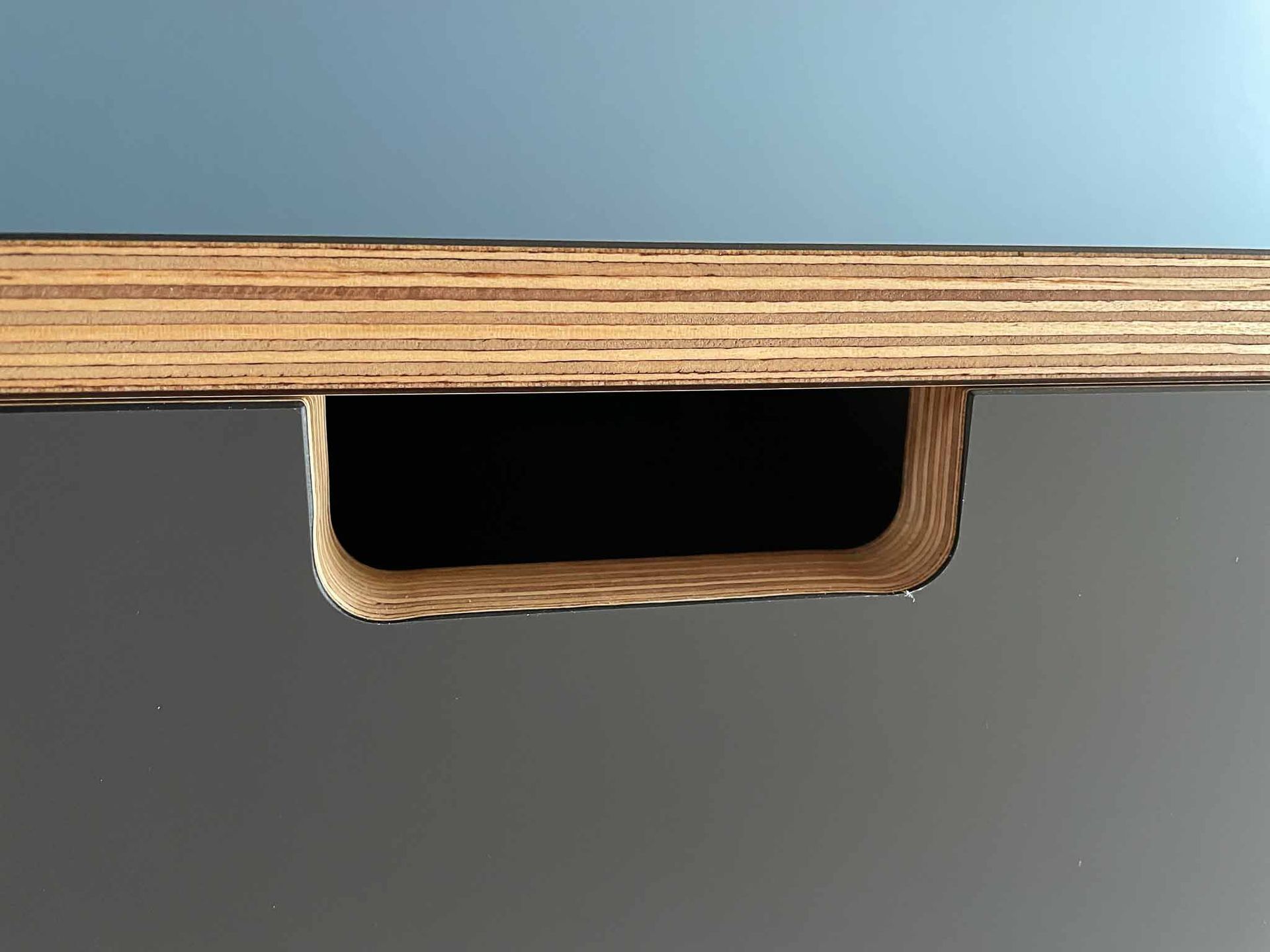 Nahaufnahme eines rechteckigen Ausschnitts in einer dunkelgrauen, holzgeschichteten Oberfläche.