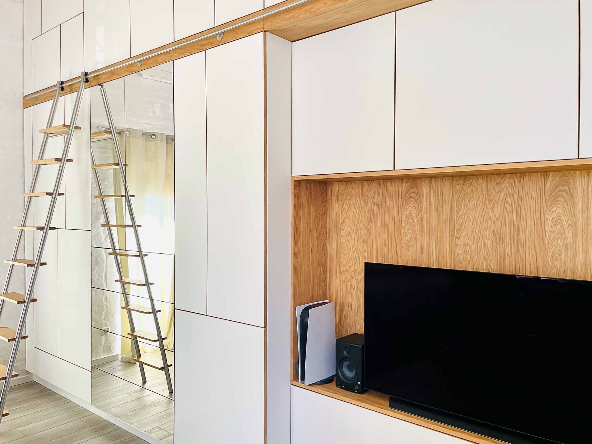 Weißes Einbau-Schrankmöbel mit Fernseher, Holzakzent und einer Leiter auf Schienen.
