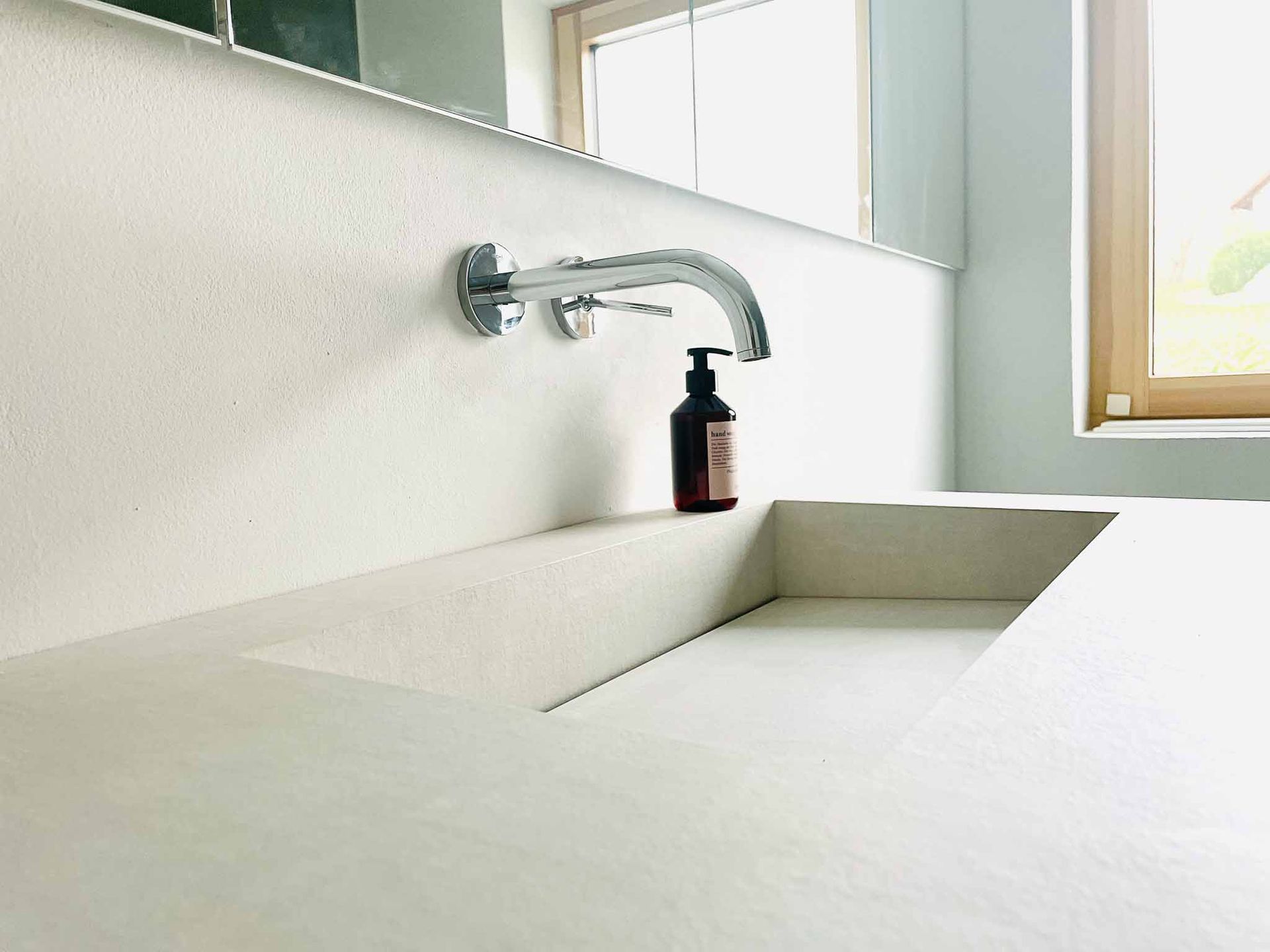 Modernes Badezimmer mit Waschbecken in Betonoptik, Chromhahn und Seifenspender.