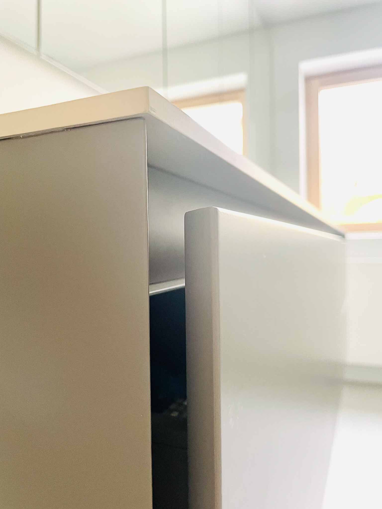 Nahaufnahme eines hellgrauen Schranks mit offener Tür, die Licht reflektiert. Fenster im Hintergrund.