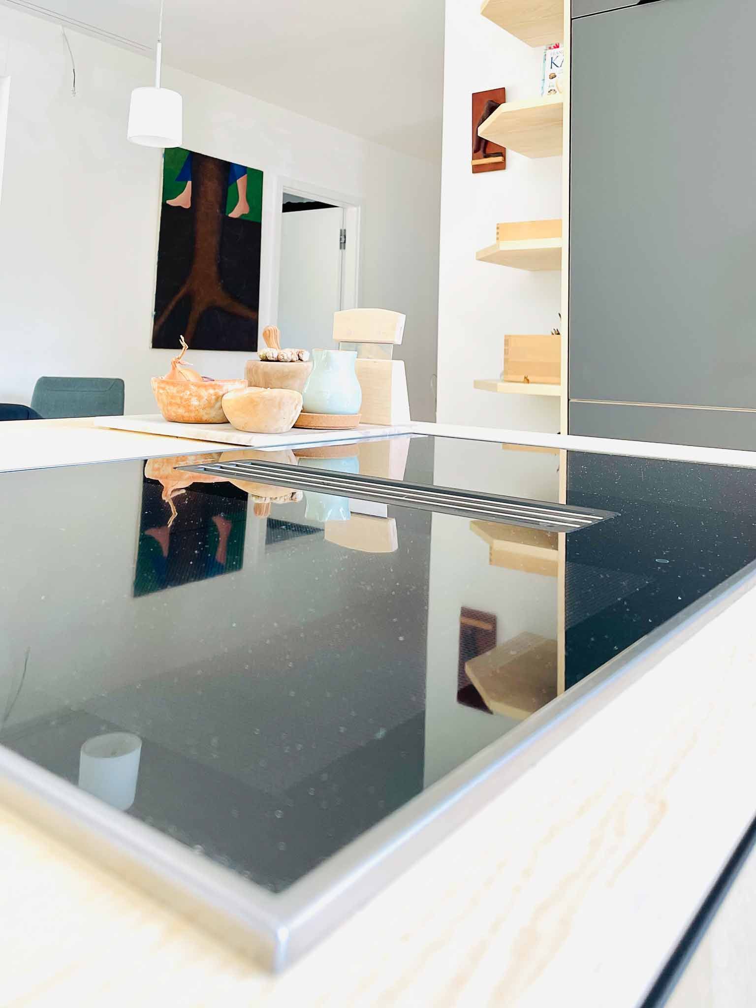 Küche mit reflektierendem schwarzem Kochfeld, weißer Deckenleuchte und Regalen.