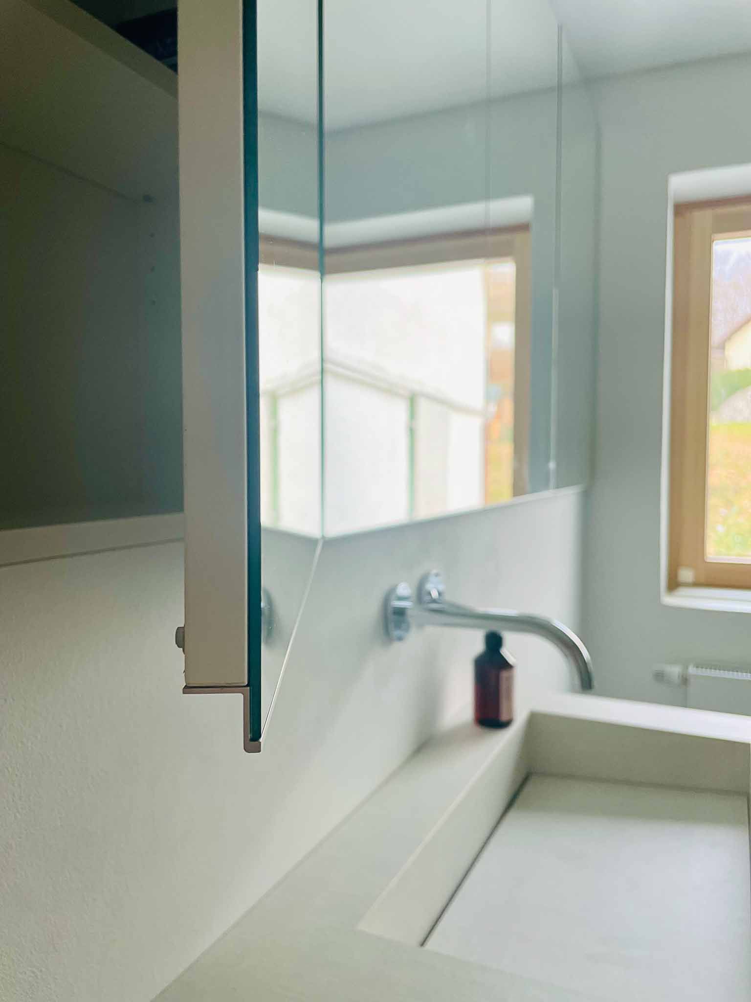 Badezimmer mit Spiegelschrank, weißem Waschbecken, Chromhahn und kleiner brauner Flasche.