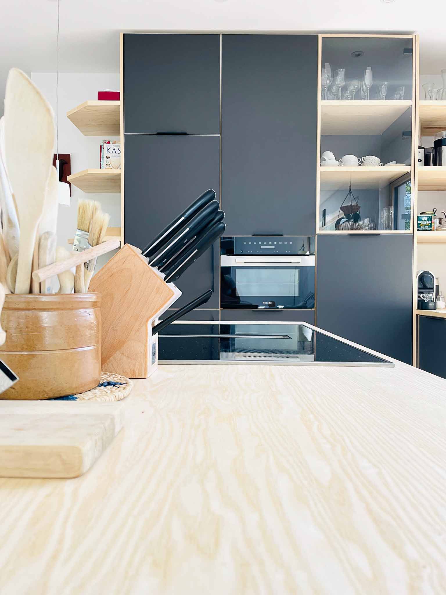 Küche mit Holztheke und dunklen Schränken. Messer, Besteck und Mikrowelle sind sichtbar.