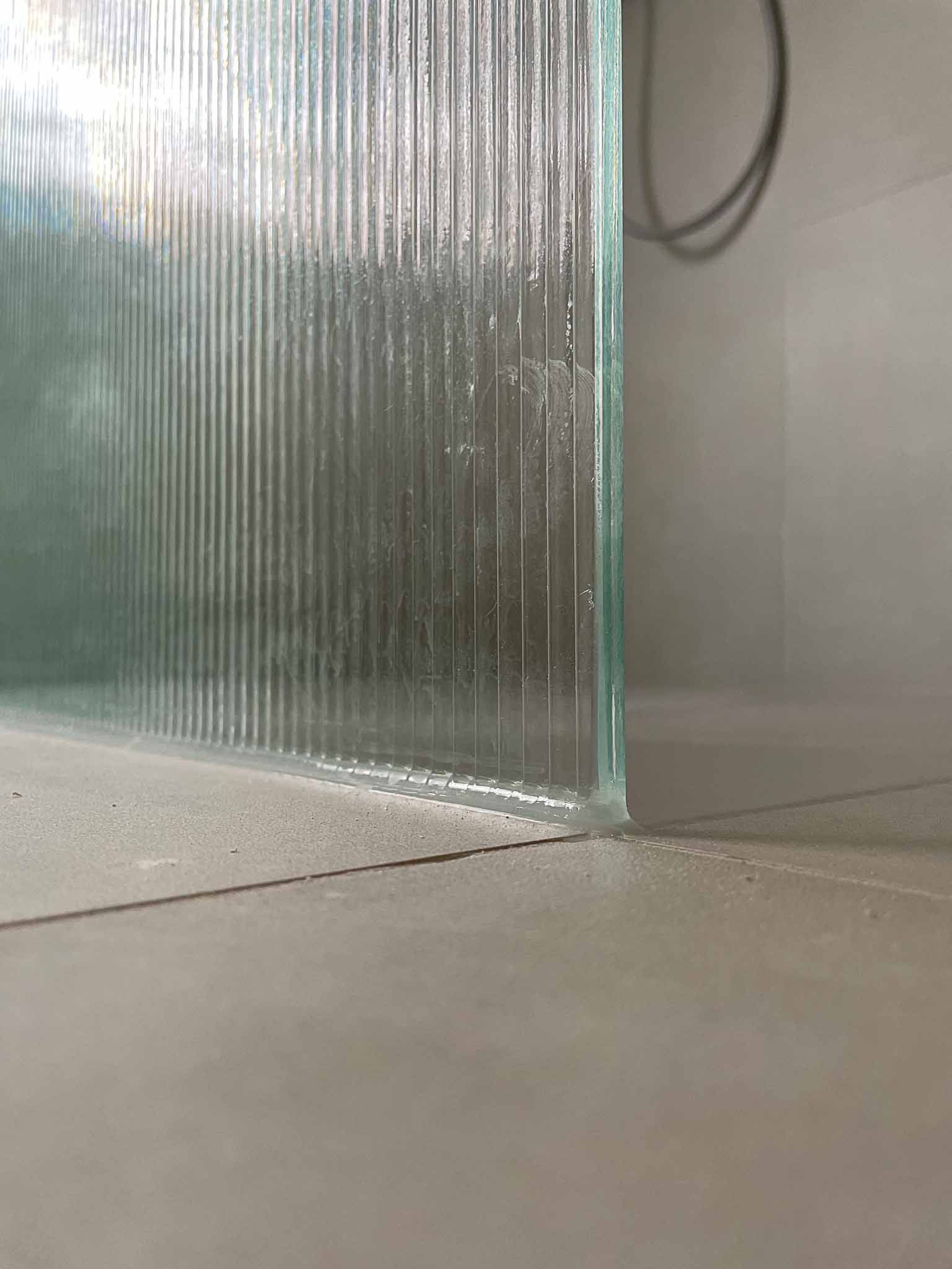 Duschwand aus strukturiertem Glas auf hellgrauem Fliesenboden.