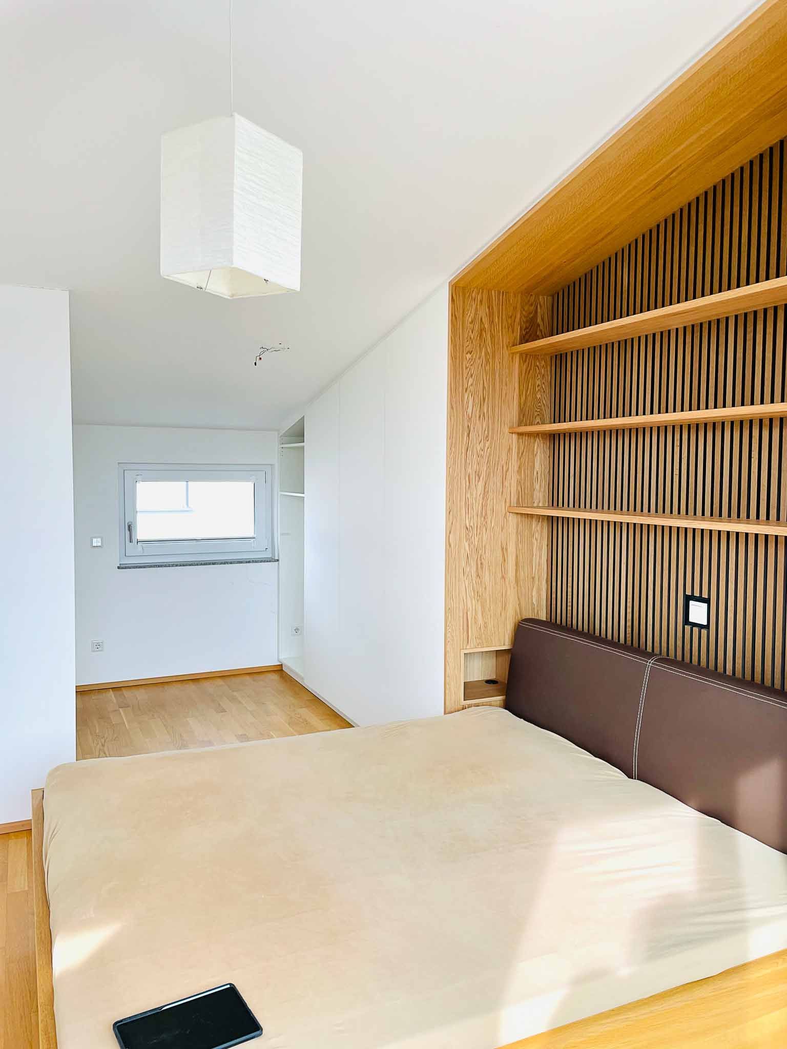 Schlafzimmer mit Bett, Regalen, gemusterter Wand und Fenster.