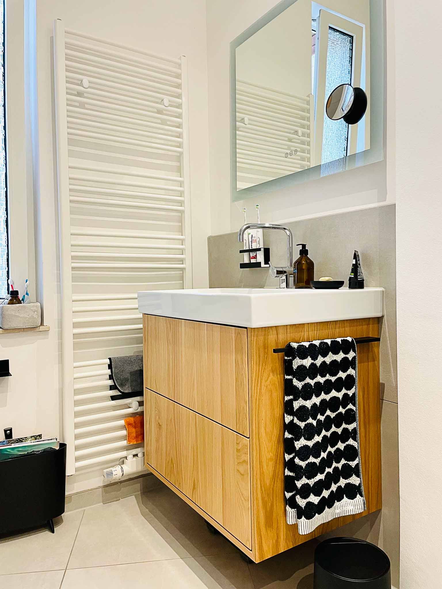 Badezimmer mit Holzwaschtisch, weißer Arbeitsplatte, großem Spiegel und gemustertem Handtuch.