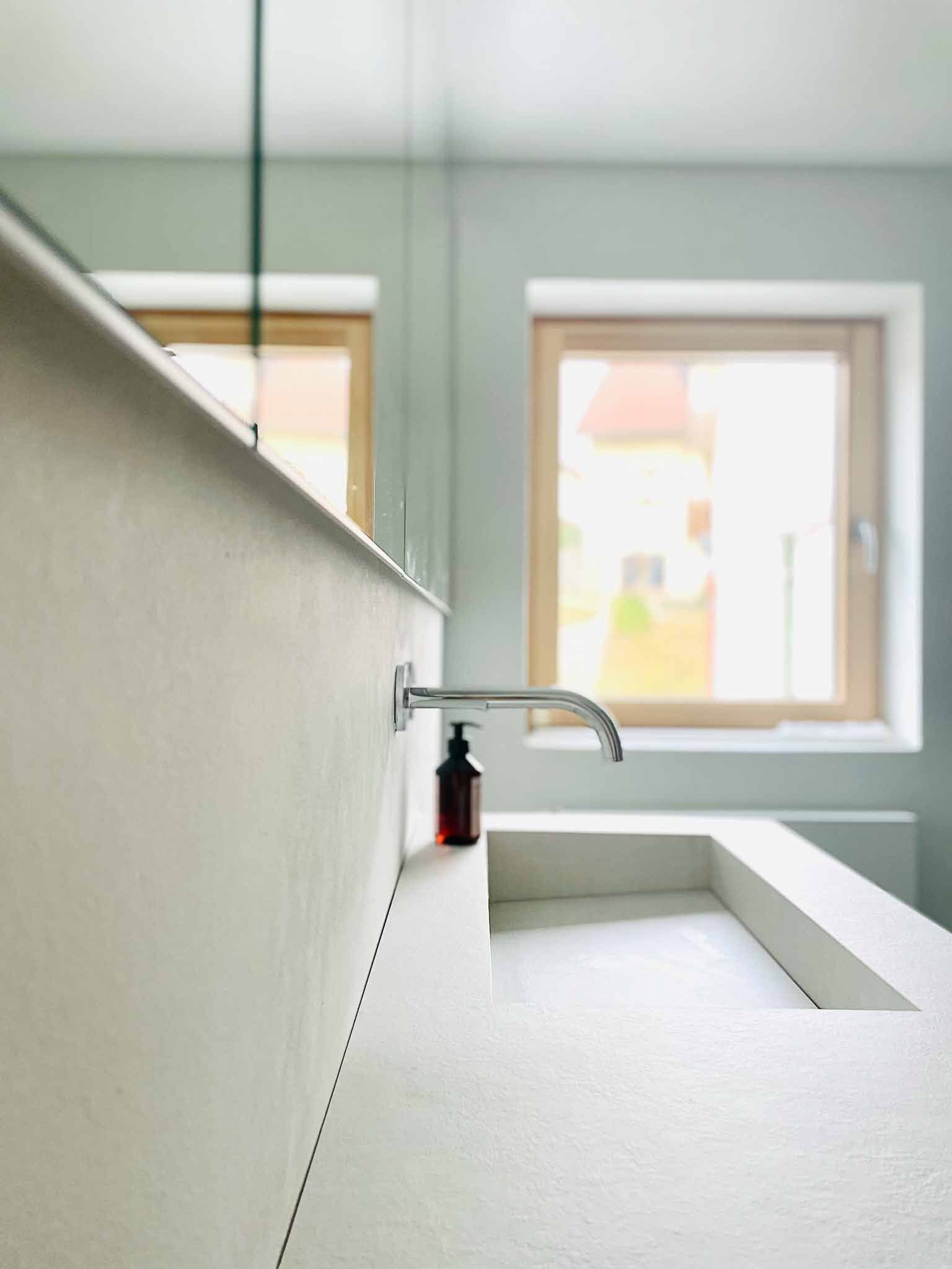 Modernes Badezimmer mit weißem Waschbecken, Chromhahn und Seifenspender am Fenster.