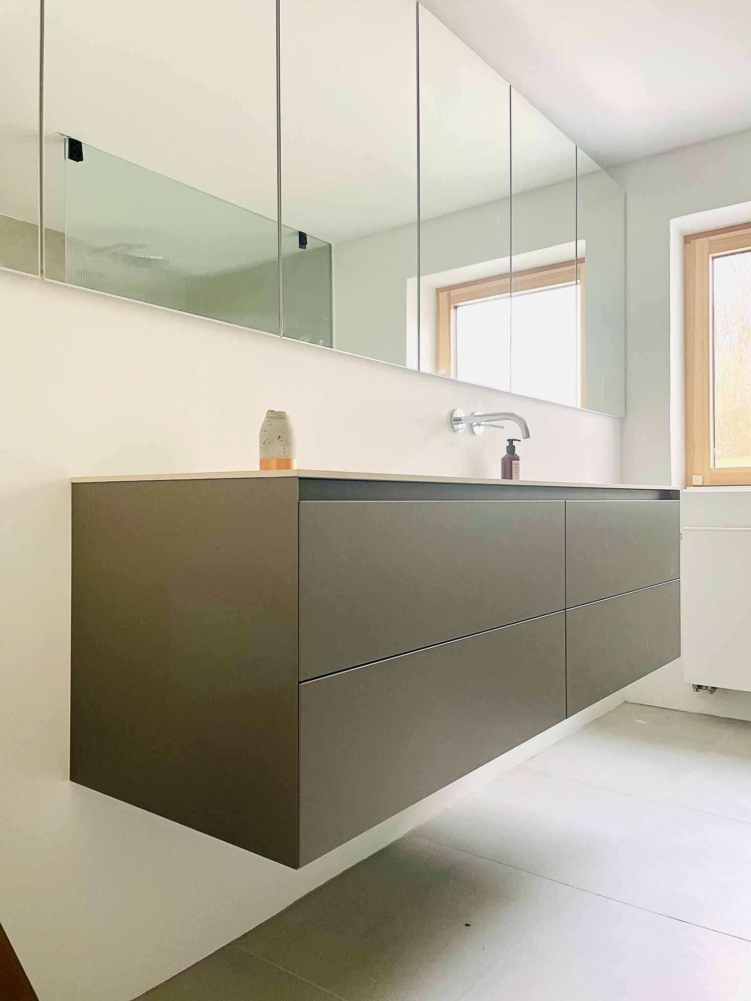 Modernes Badezimmer mit schwebendem grauen Waschtisch, großem Spiegel und Fenstern mit Holzrahmen.