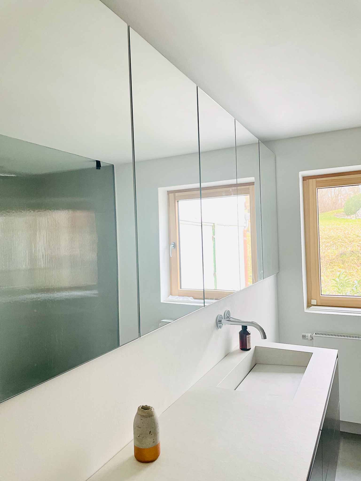 Modernes Badezimmer mit einem großen Spiegel mit gewellten Kanten über einer weißen Arbeitsplatte mit eingebautem Waschbecken.