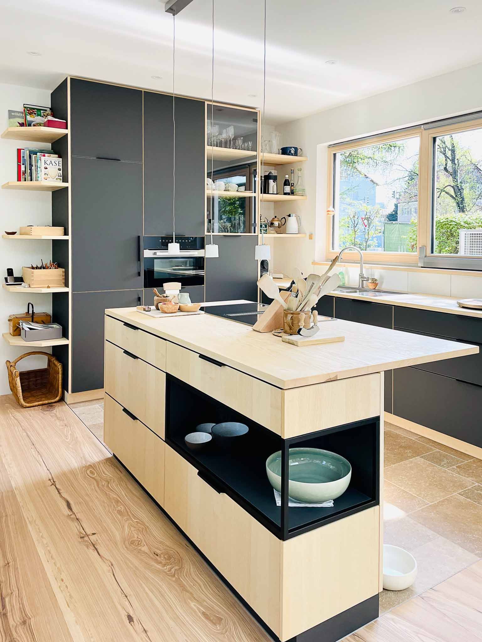 Moderne Küche mit Kochinsel und dunkelgrauen Schränken, hellen Holzakzenten, offenen Regalen und Fenster.