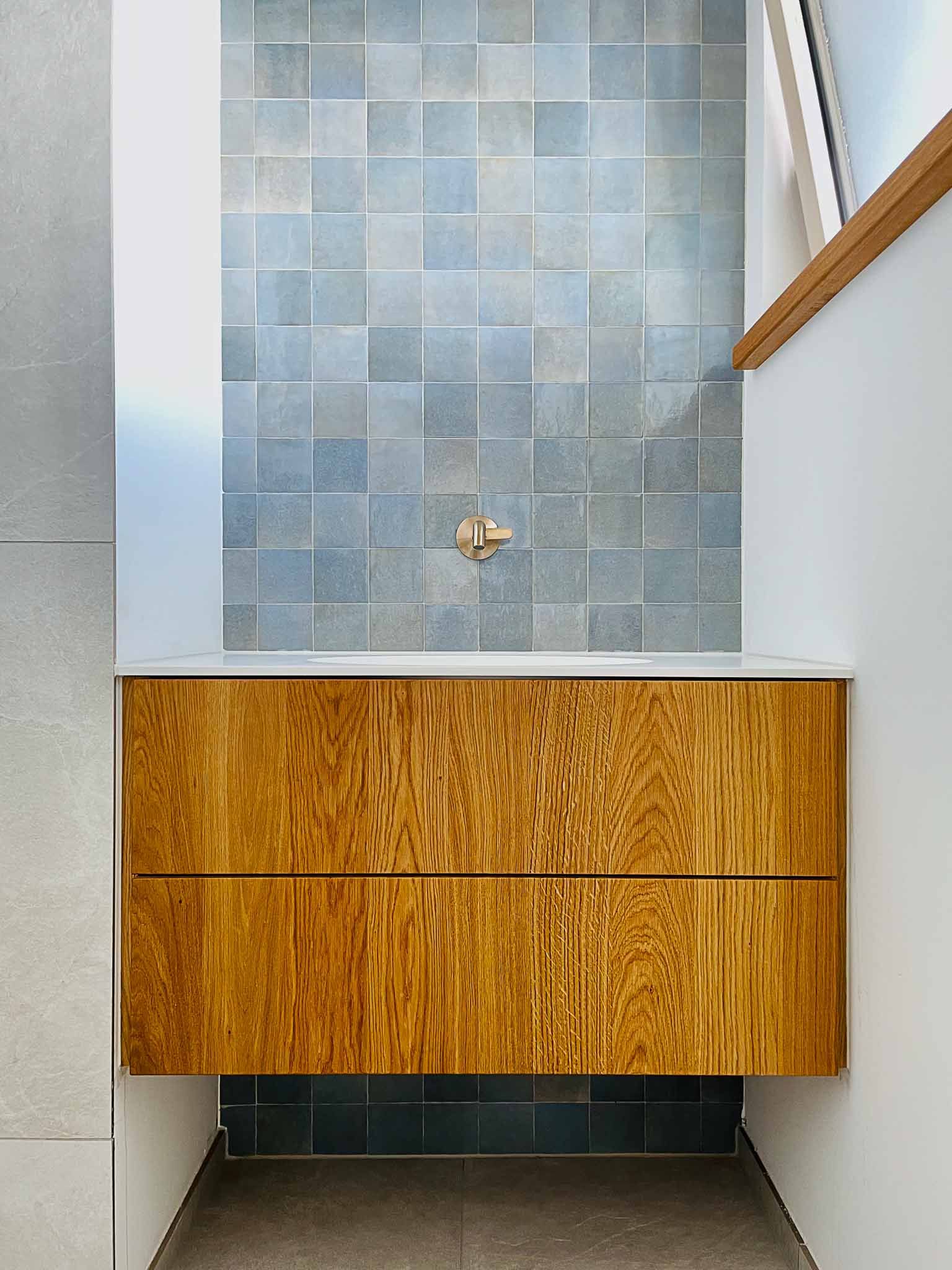 Badezimmerwaschtisch aus Holz mit zwei Schubladen, vor blau gefliester Wand, Ecke eines Badezimmers.