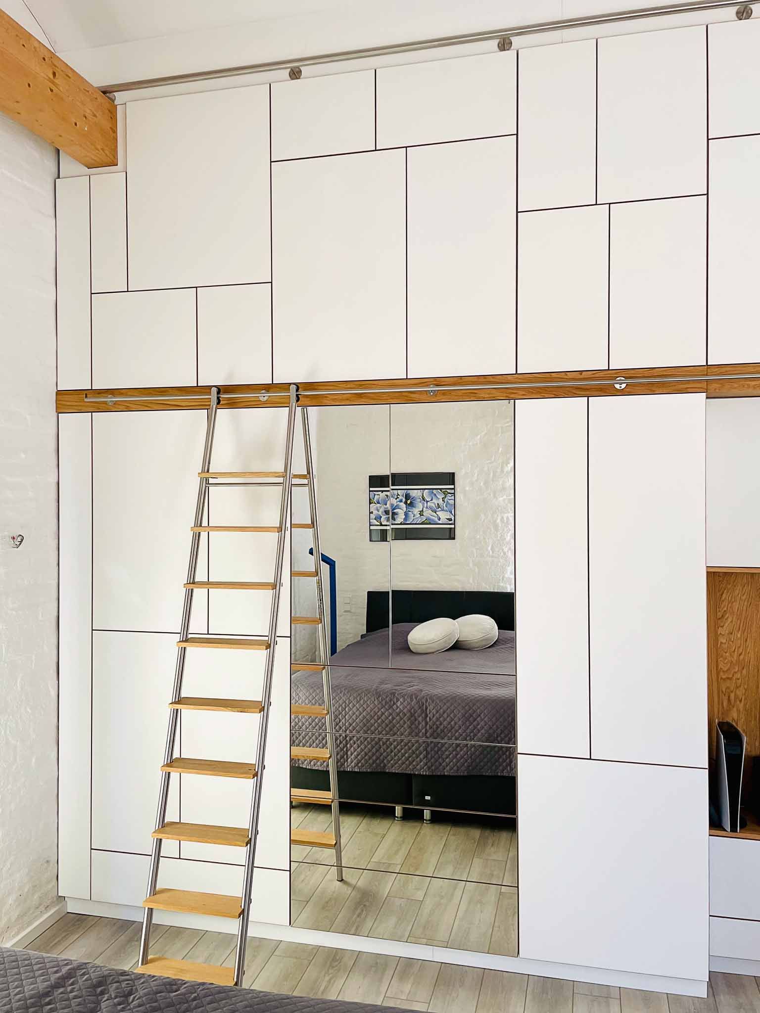 Hochbett mit weißen Wandpaneelen und einer Leiter. Ein Spiegel reflektiert ein Bett.
