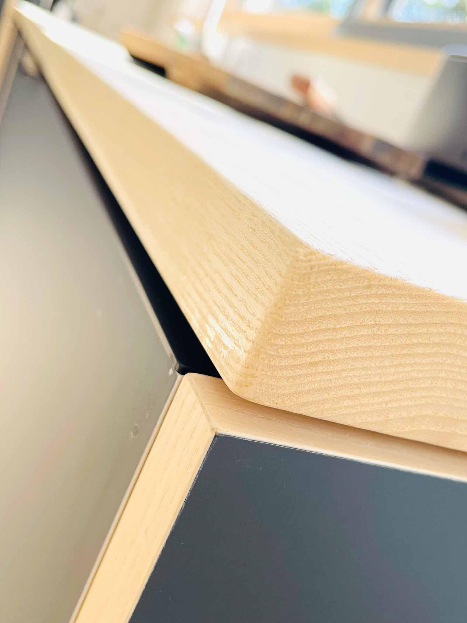 Holzbrett mit abgewinkelter Kante auf einem dunklen Schrank.
