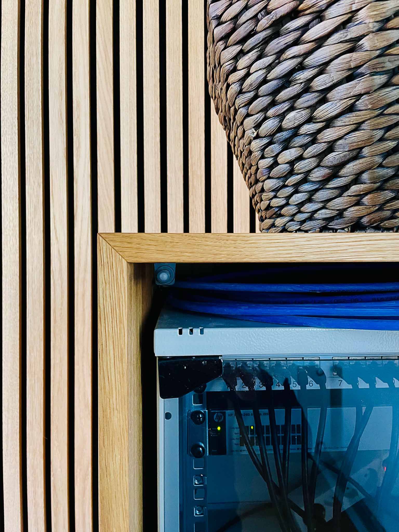 Holzverkleidung mit einem gerahmten Server-Rack, blauen Kabeln und einem geflochtenen Korb.