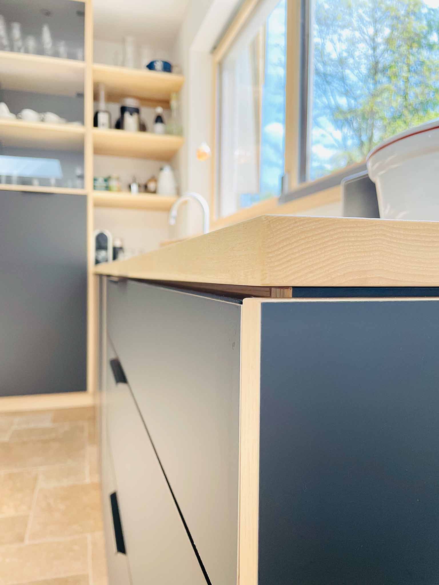 Moderne Küche mit dunkelblauen Schränken, Holzarbeitsplatten und hellen Holzregalen.