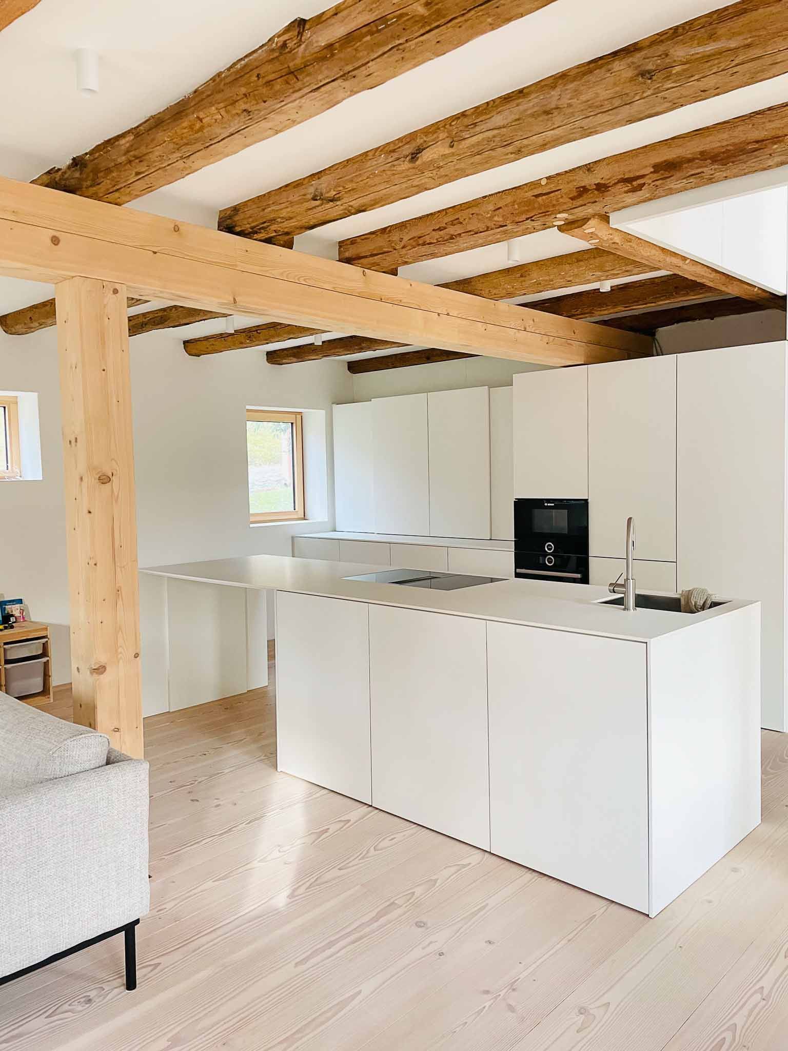 Strahlend weiße Küche mit Holzbalken, Kochinsel und Einbaugeräten.