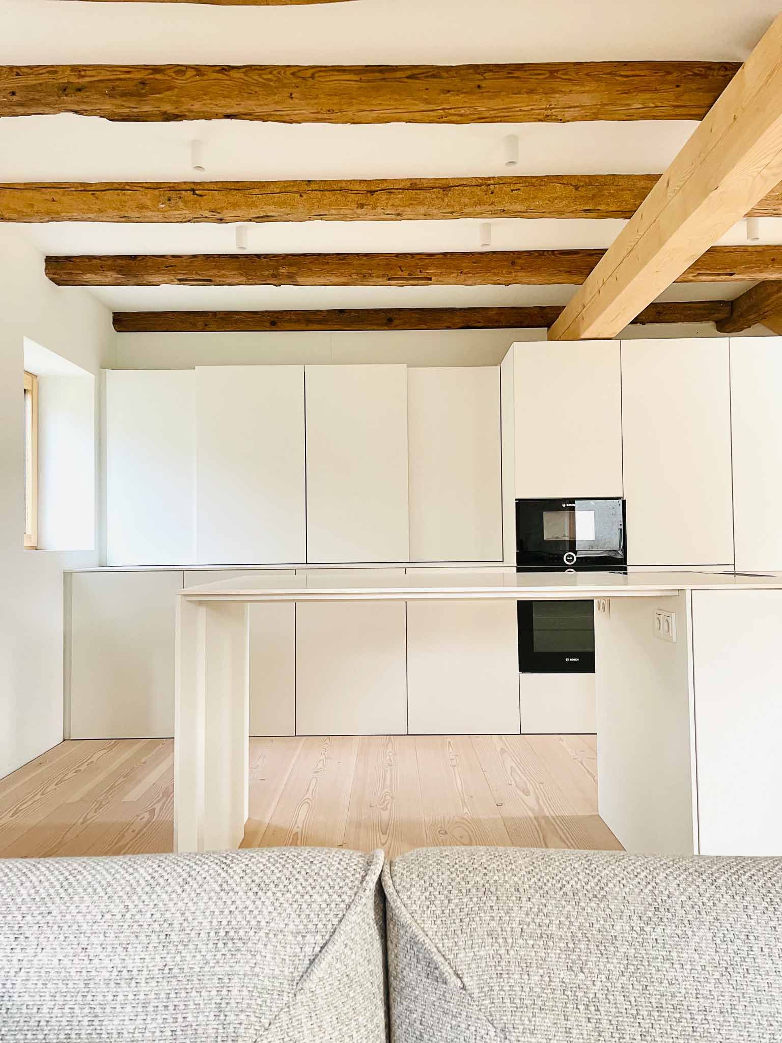 Moderne weiße Küche mit hellen Holzbalken und -boden, minimalistisches Design.