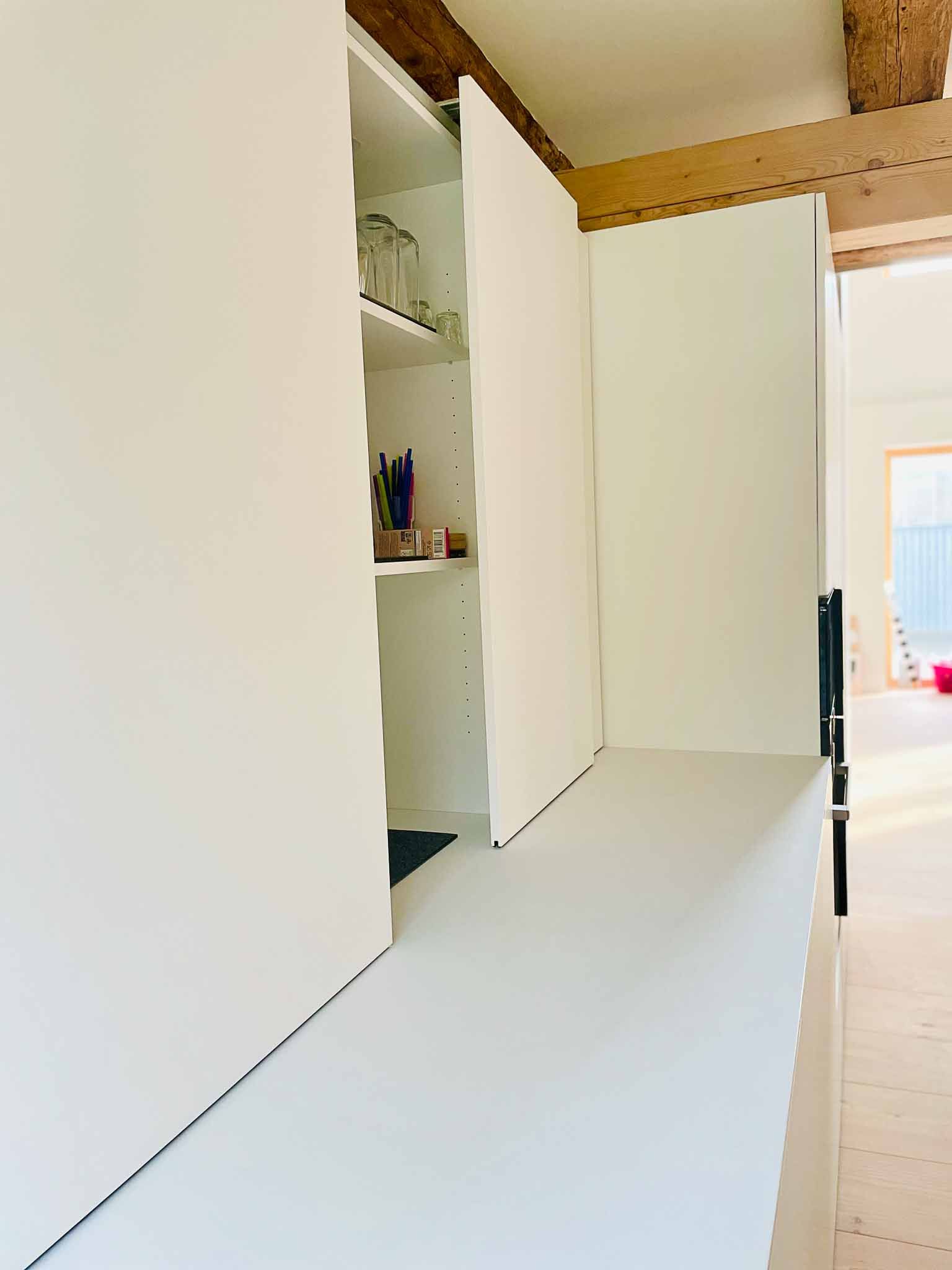 Weiße Schiebetüren öffnen sich und geben den Blick auf Regale und Gegenstände frei. Der Raum ist hell.