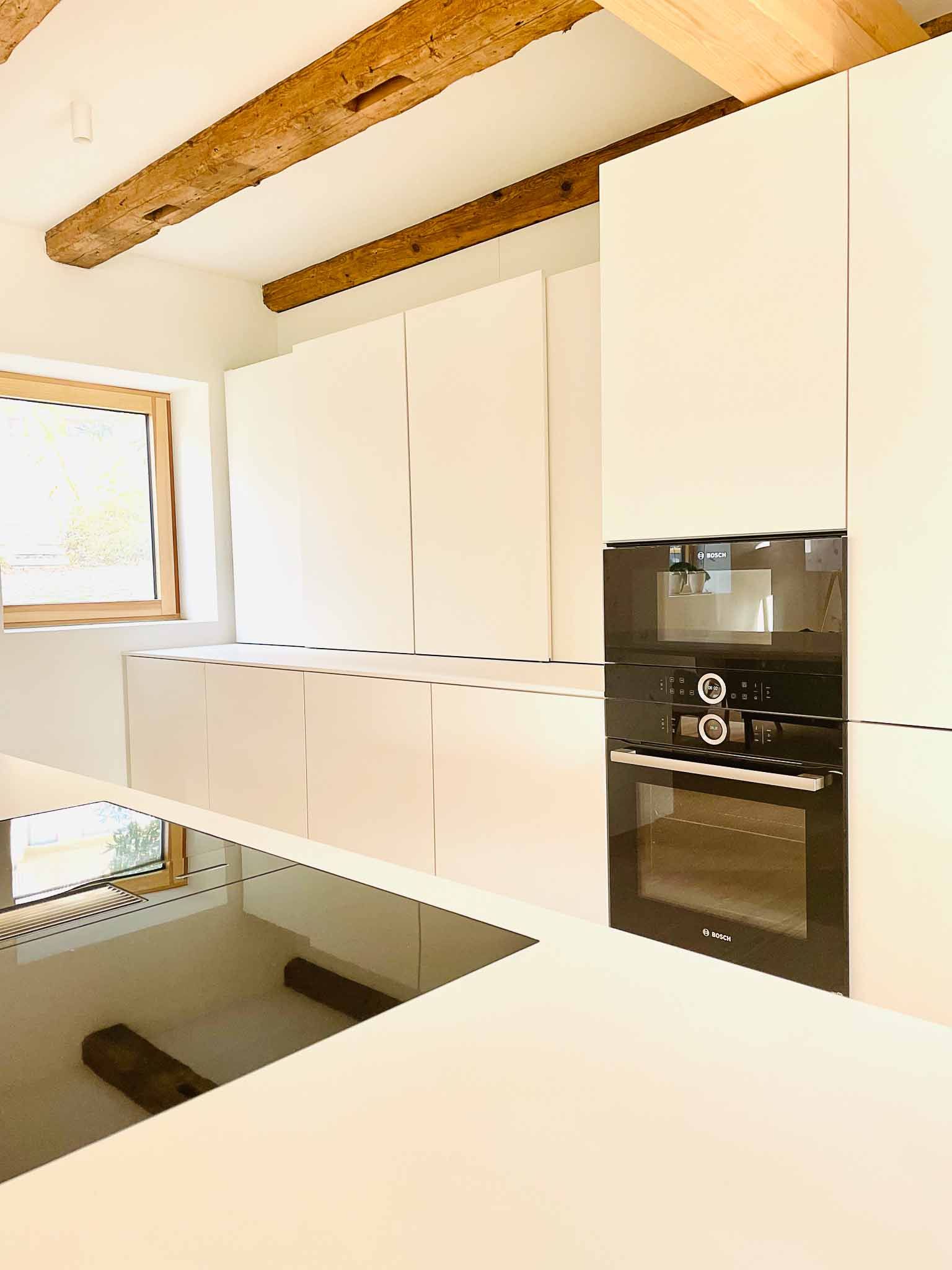 Moderne weiße Küche mit eingebautem Ofen und freiliegenden Holzbalken.