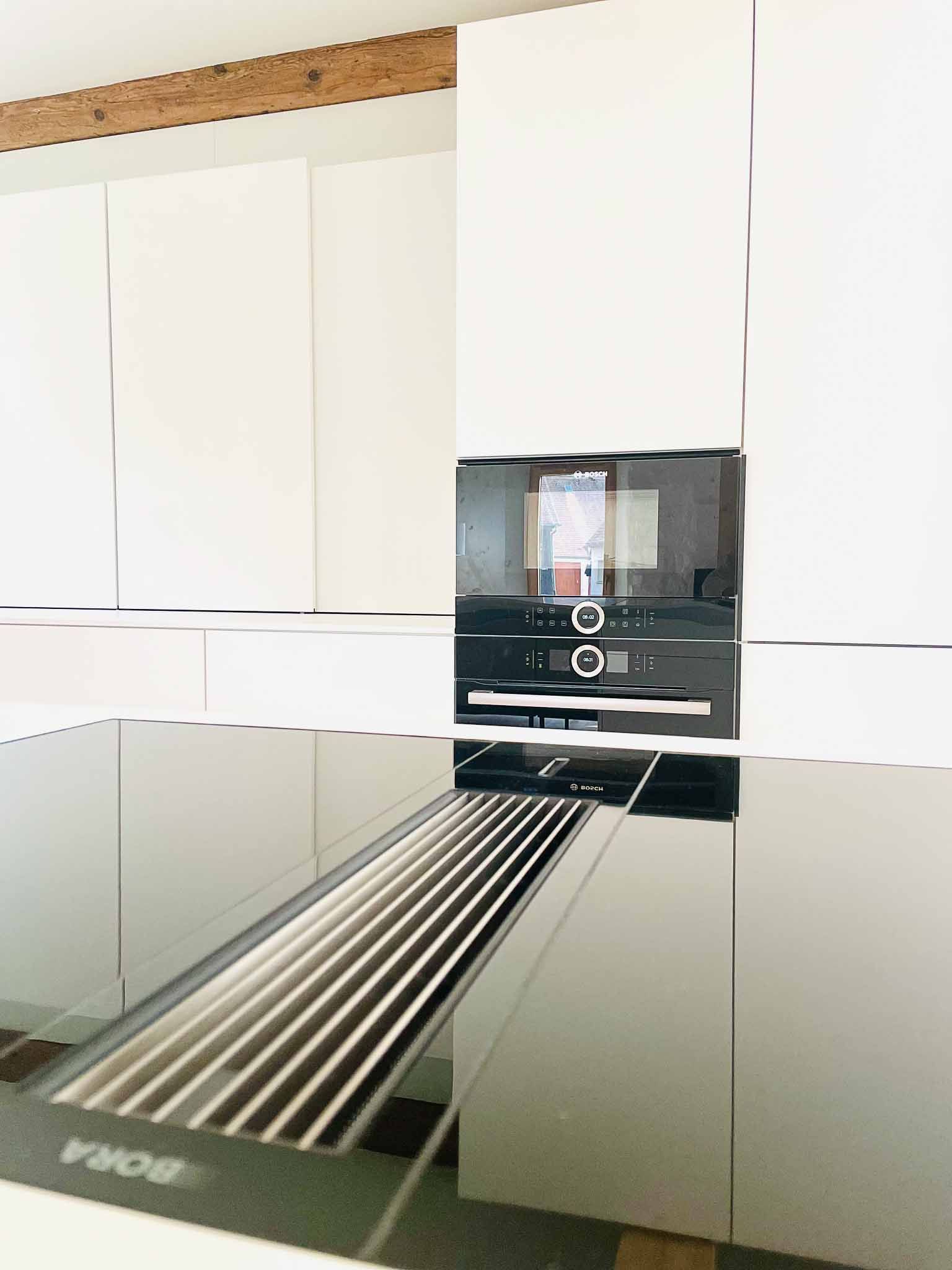 Moderne Küche mit schwarzem Kochfeld und integrierter Dunstabzugshaube. Schwarzer Backofen in einem weißen Schrank.