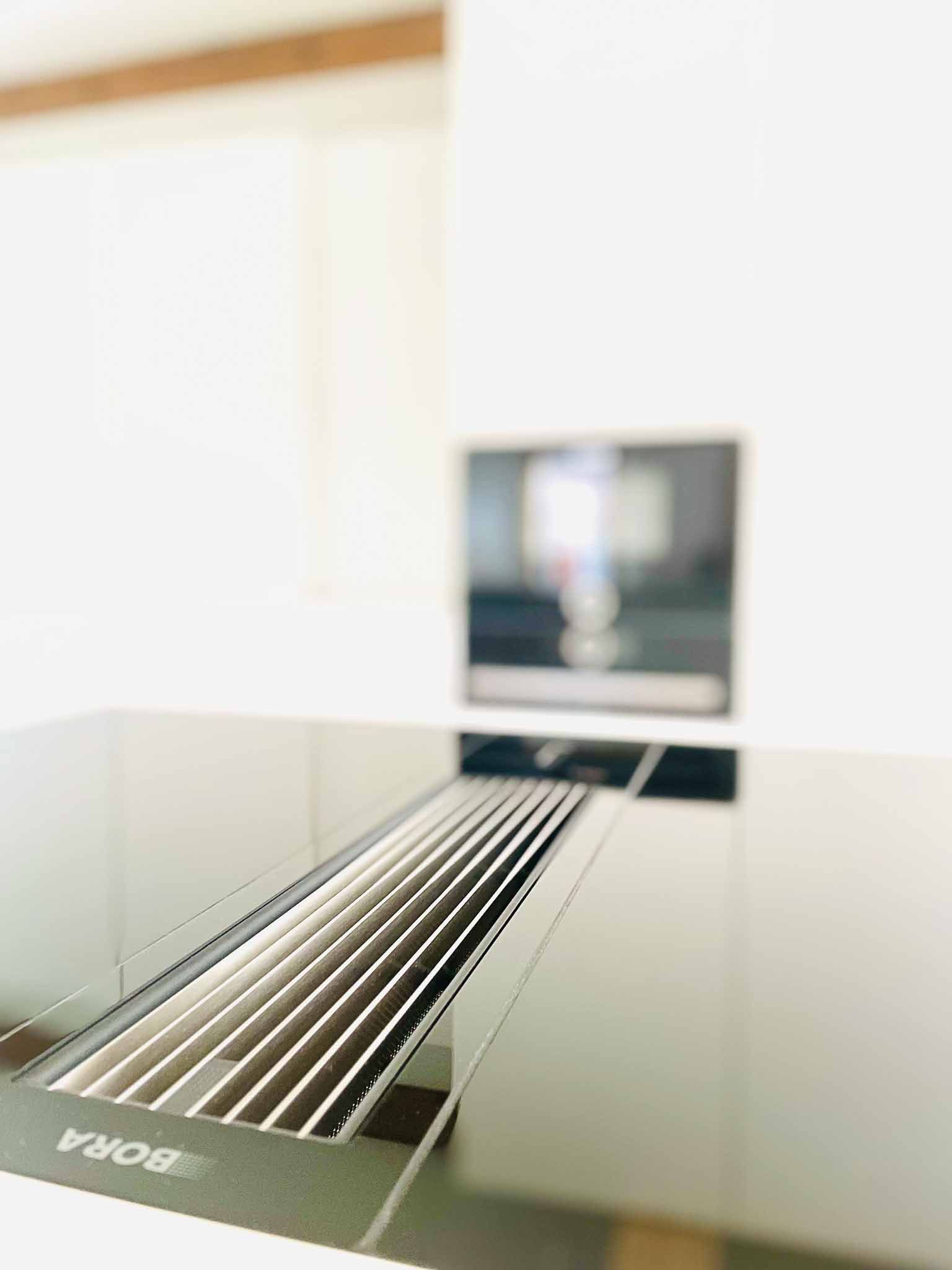 Schwarzes Küchenkochfeld mit integrierter Entlüftung, unscharfer Hintergrund mit Bildschirm.