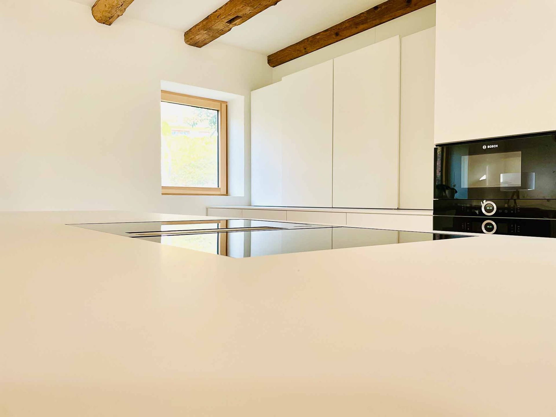 Eine moderne Küche mit weißen Schränken, einem Fenster und einem Backofen.