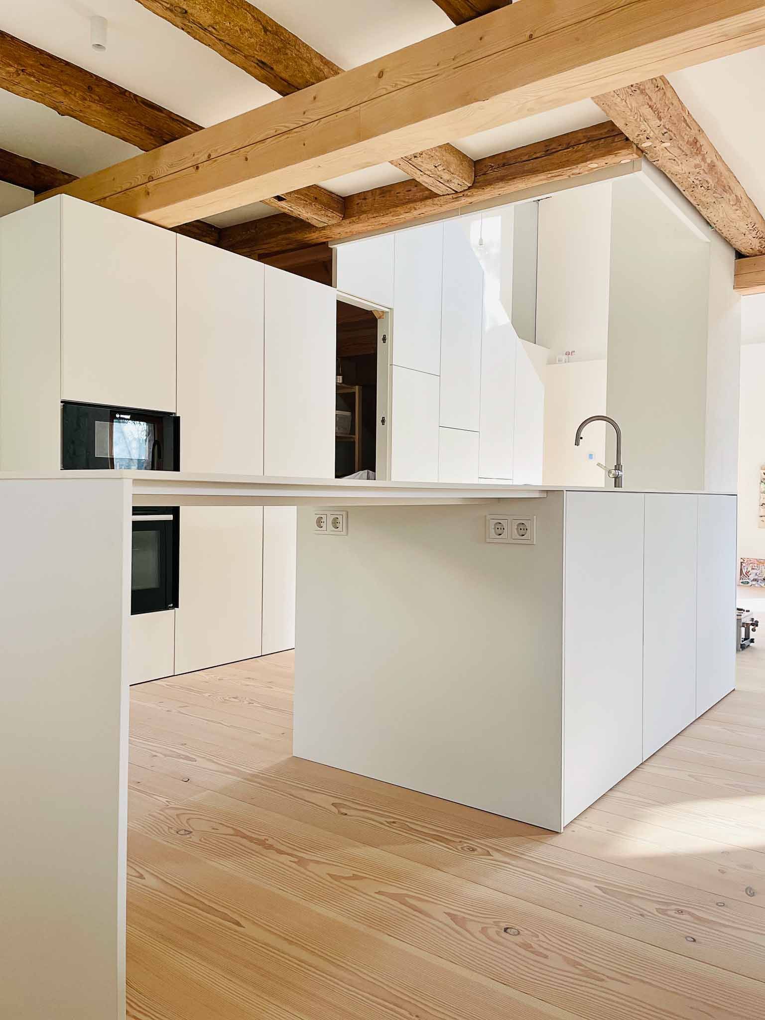 Moderne weiße Küche mit Kochinsel, Holzbalken und hellem Holzboden.