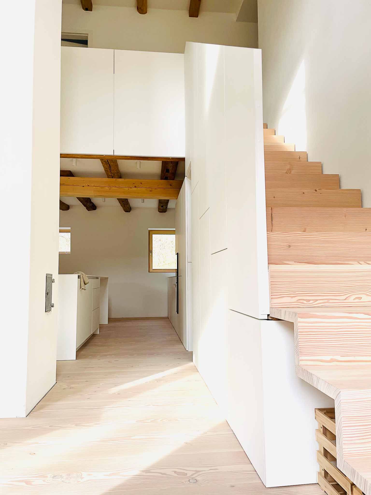 Innenansicht eines im Bau befindlichen Gebäudes; unfertige Holztreppen und weiße Wände.