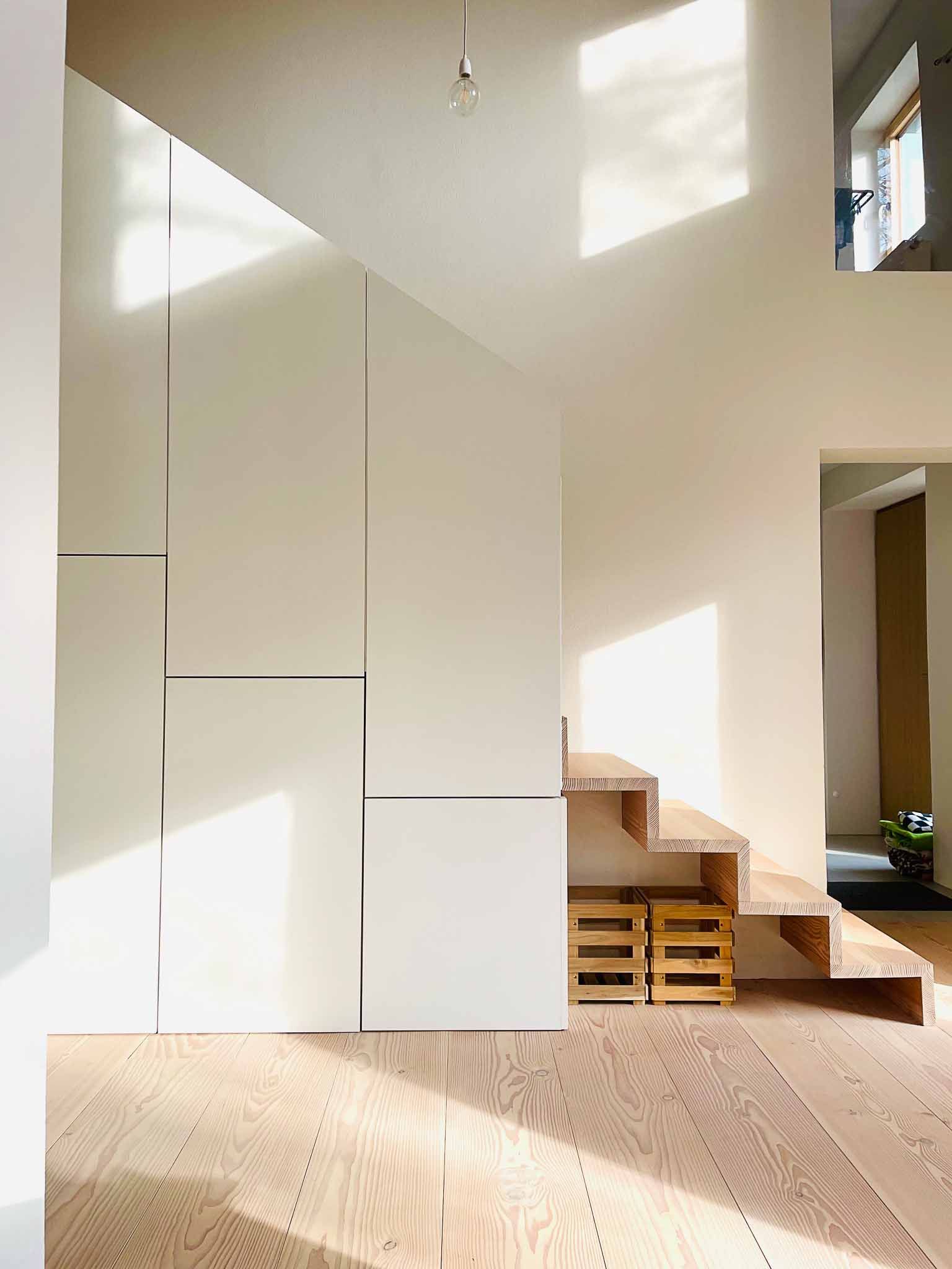 Hell erleuchteter Innenraum mit Holztreppe, weißen Wänden und Sonnenlicht.