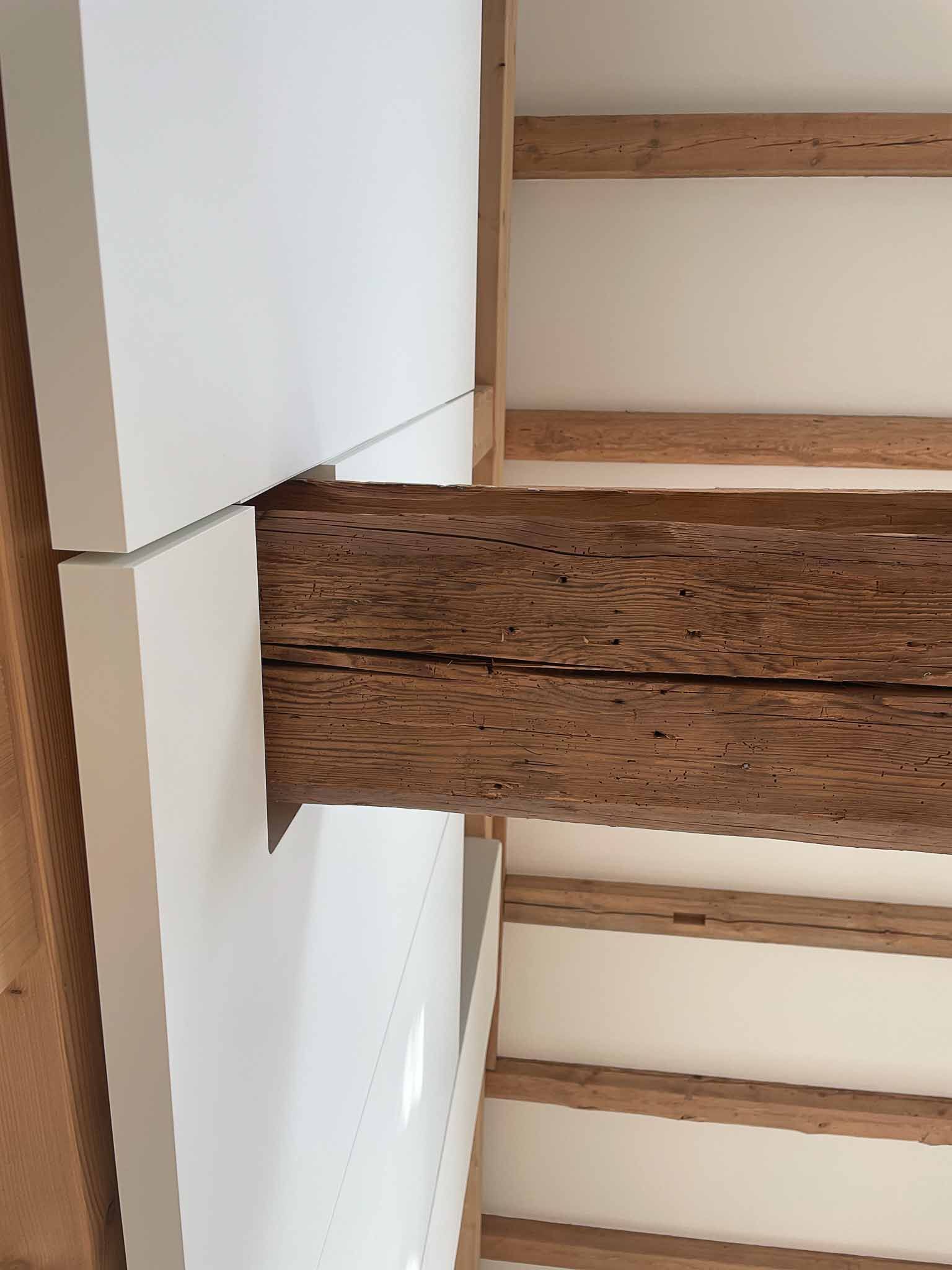 Aus der weißen Wand ragt ein Holzbalken, freiliegende Deckenbalken sind sichtbar.