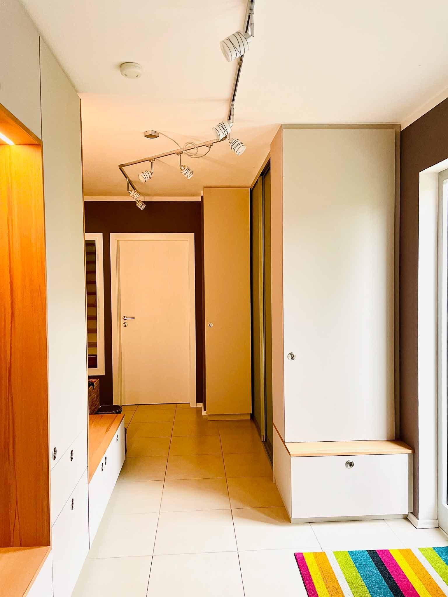Schmaler Flur mit weißen und braunen Wänden, eingebautem Stauraum und einem bunten Teppich.
