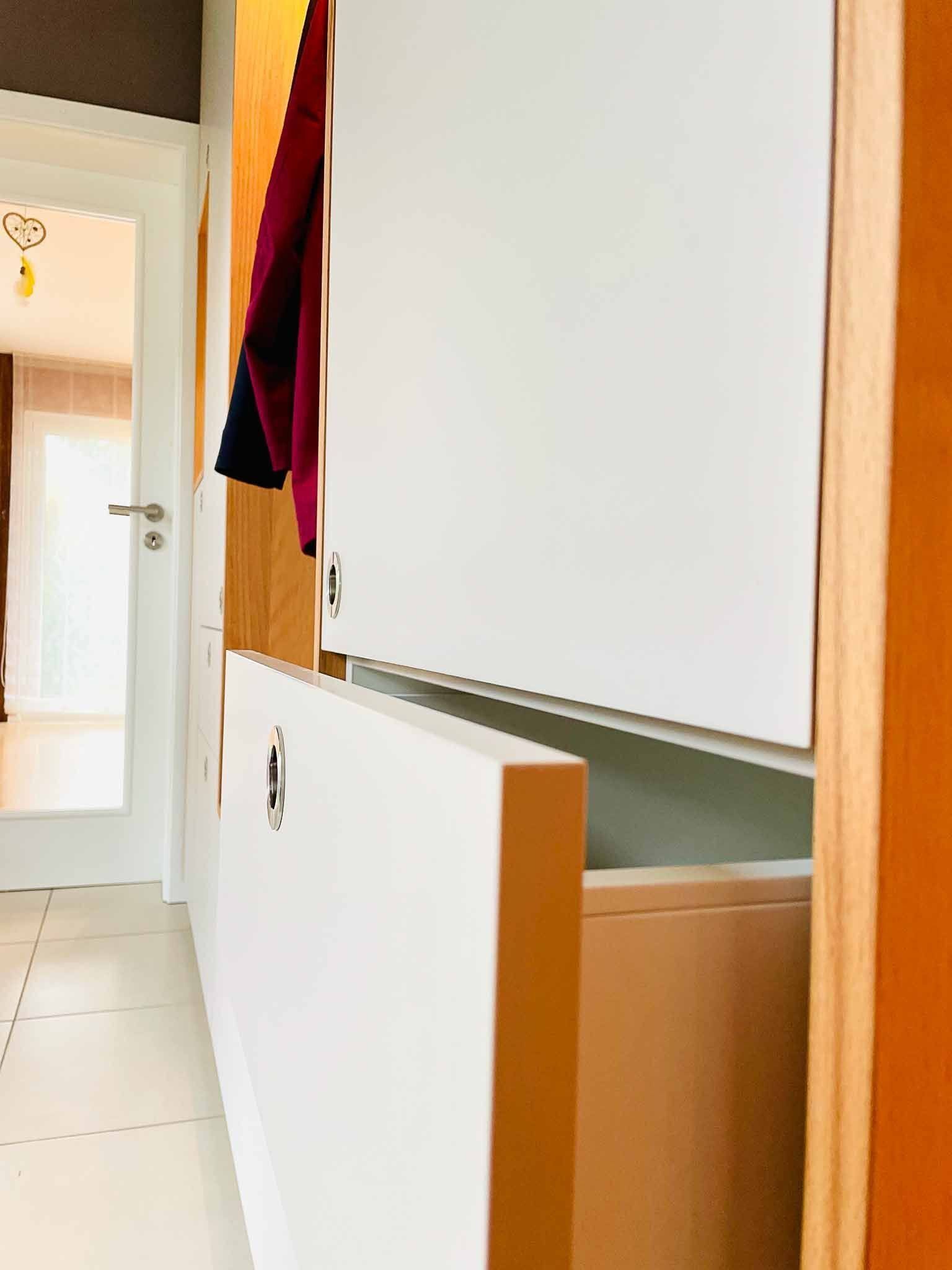 Weiße und hölzerne Schränke mit einer offenen Schublade, Blick in den Flur. In der Nähe hängt eine burgunderfarbene Jacke.