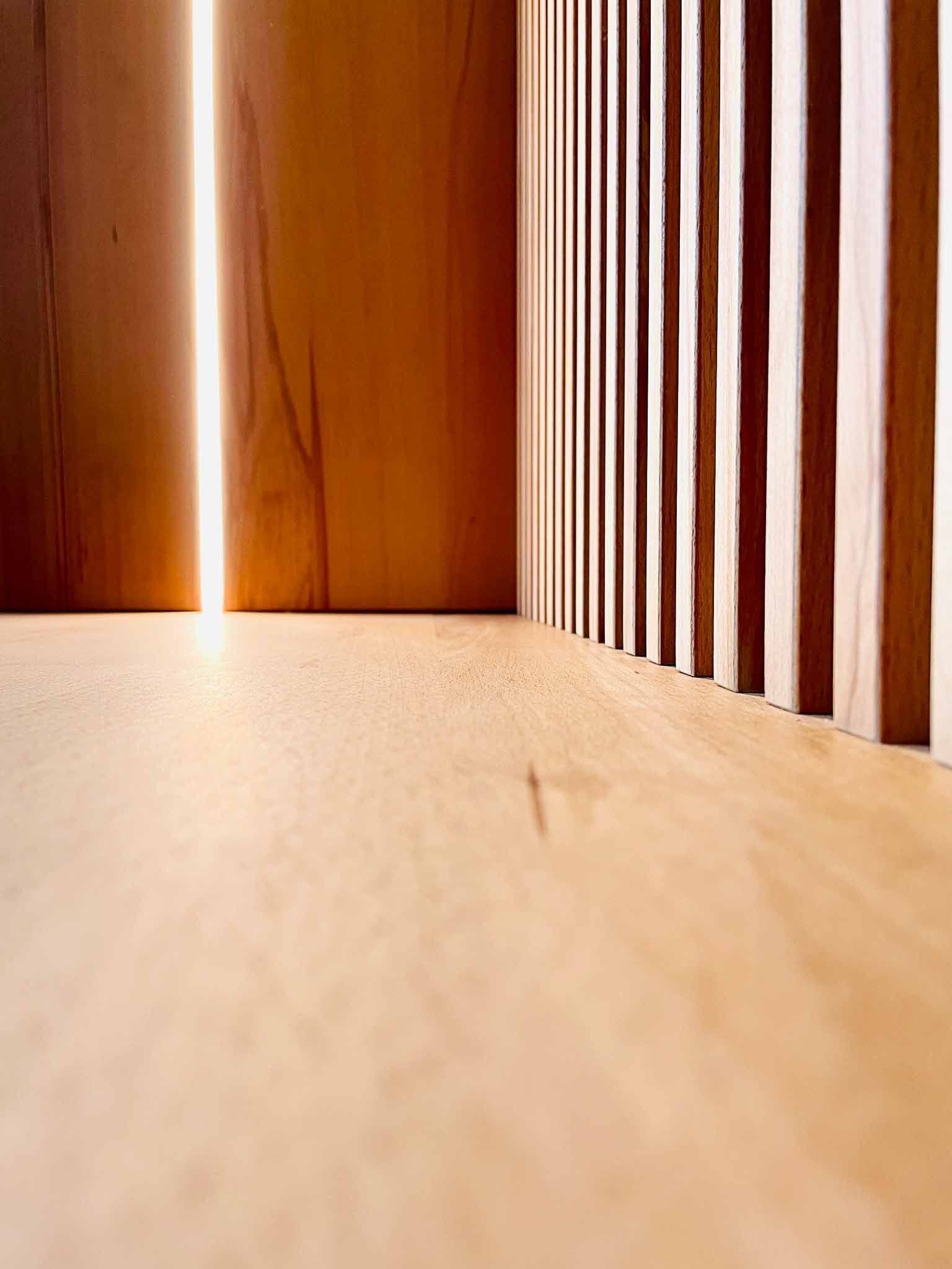 Holzlatten und -paneele, durch deren Spalt helles Licht scheint.