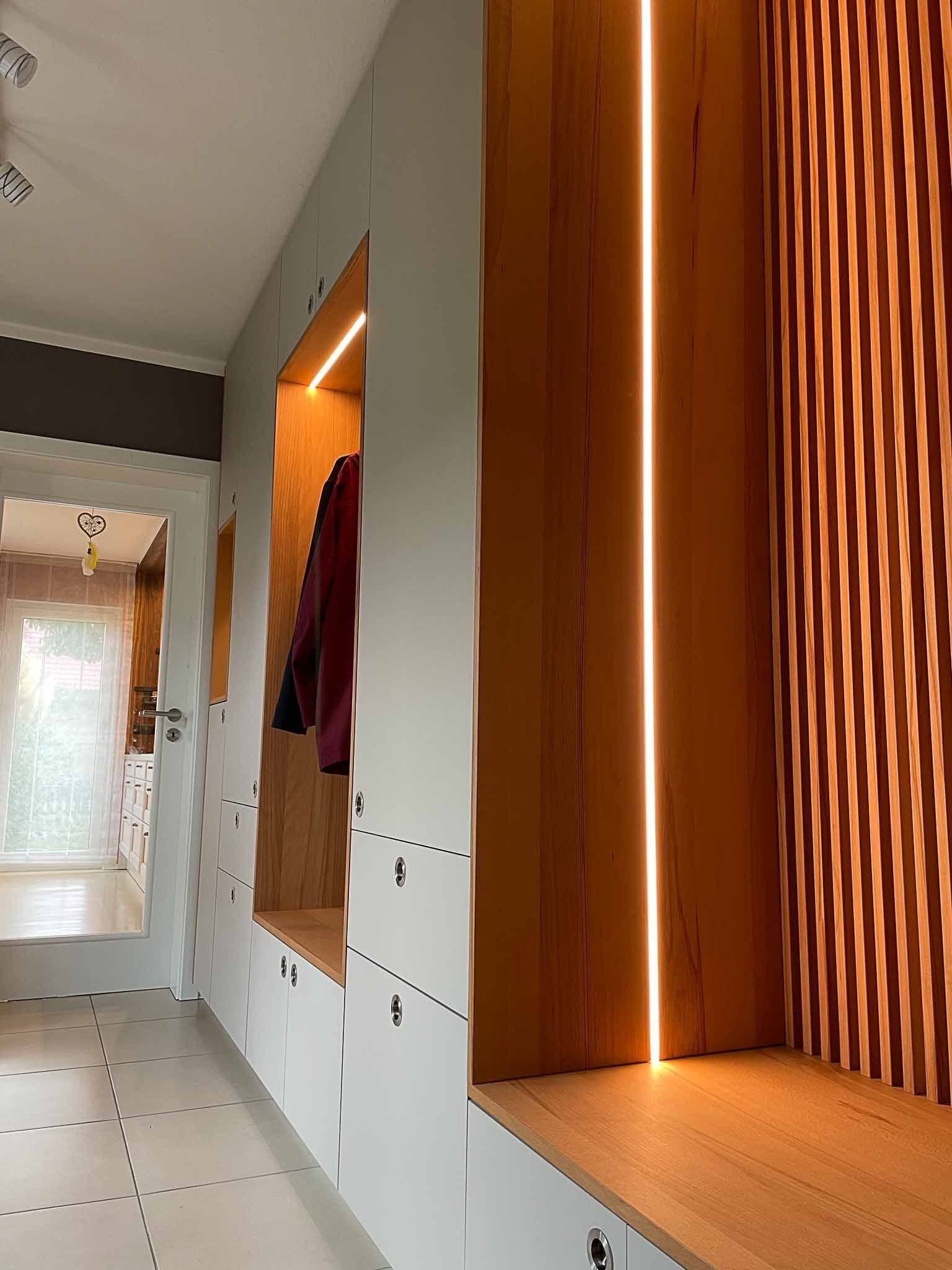 Moderner Flur mit eingebautem Stauraum aus Holz und Weiß, beleuchtet durch vertikales LED-Licht.