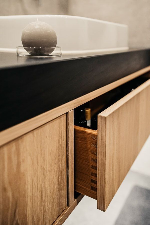 Badezimmerwaschtisch aus Holz mit offener Schublade, dunkler Arbeitsplatte und weißem Waschbecken.