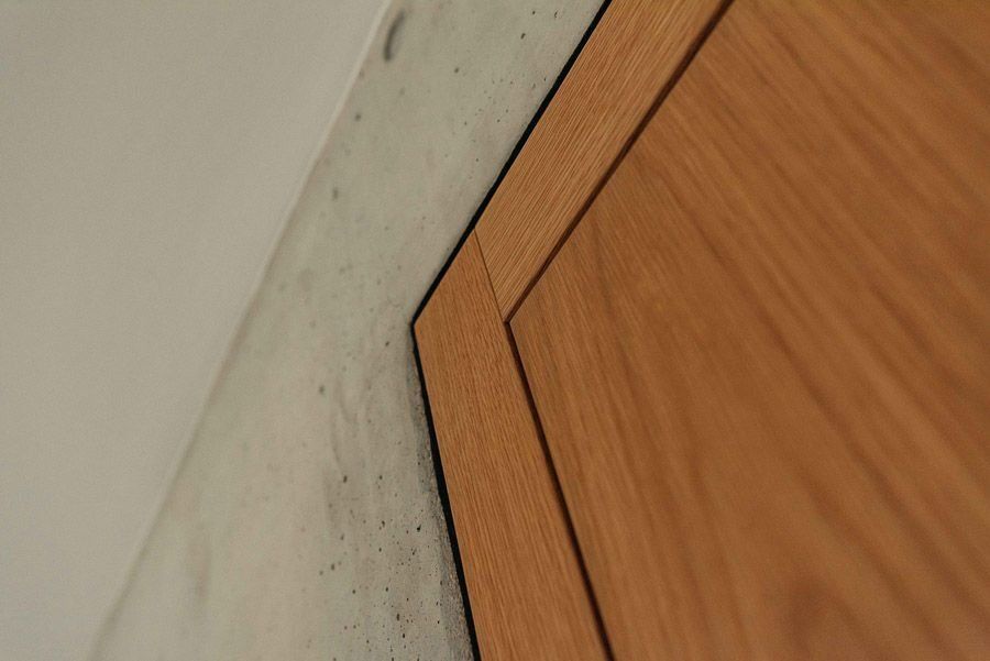 Nahaufnahme eines hellen Holztürabschnitts vor einer Betonwand. Die Ecke der Tür ist sichtbar.