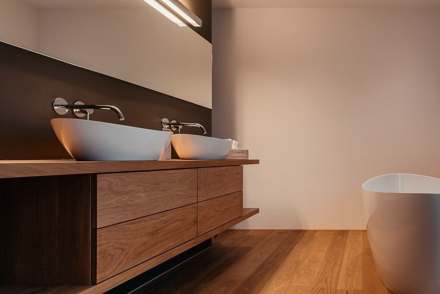 Badezimmerschrank aus Holz mit weißen Waschbecken, Spiegel und Badewanne; Holzböden.