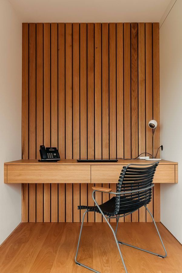 In die Wand eingebauter Holzschreibtisch mit Telefon, Tastatur, Lampe und schwarzem Stuhl.