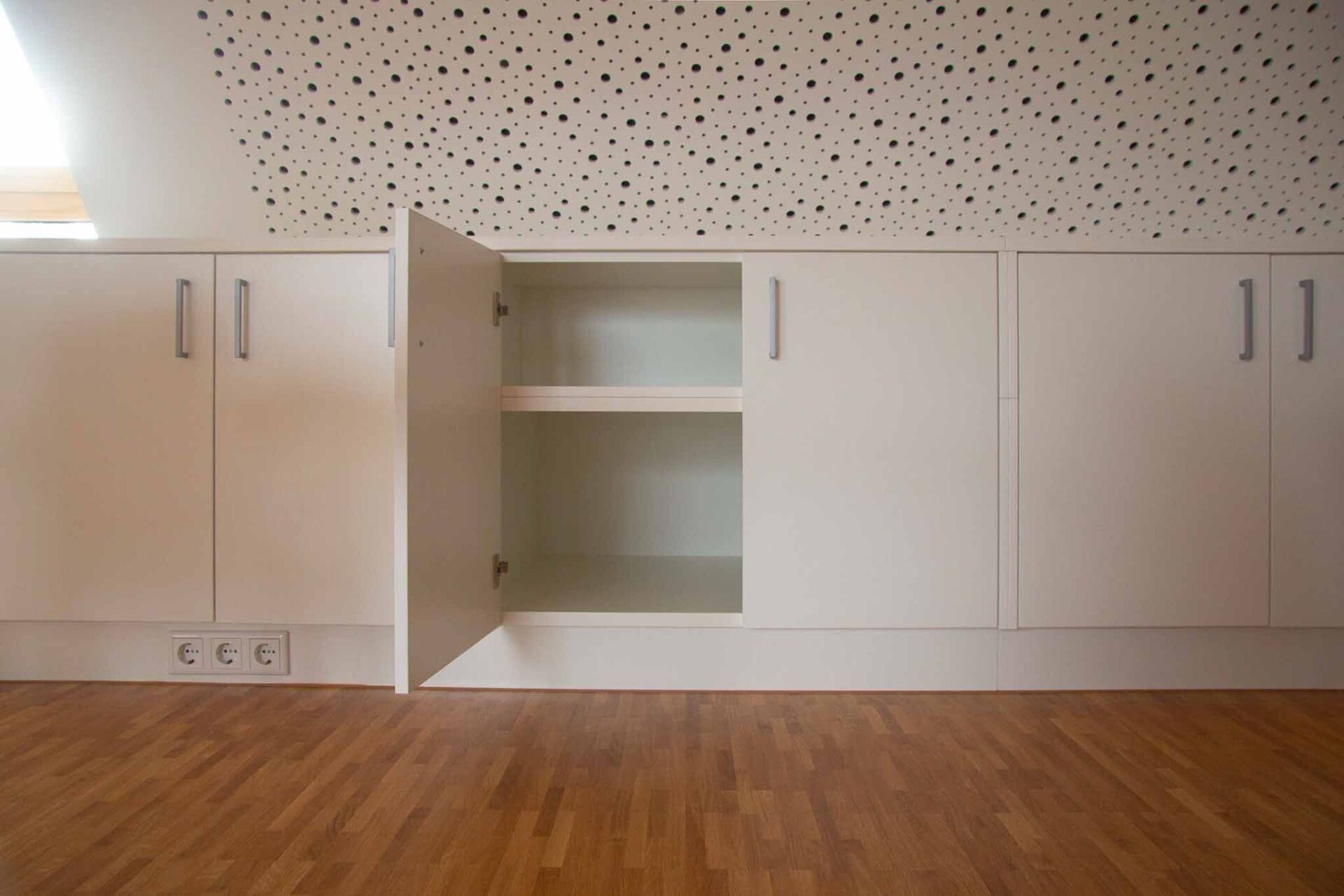 Weiße Schränke mit einer offenen Tür, in eine Wand eingebaut, über einem Holzboden.