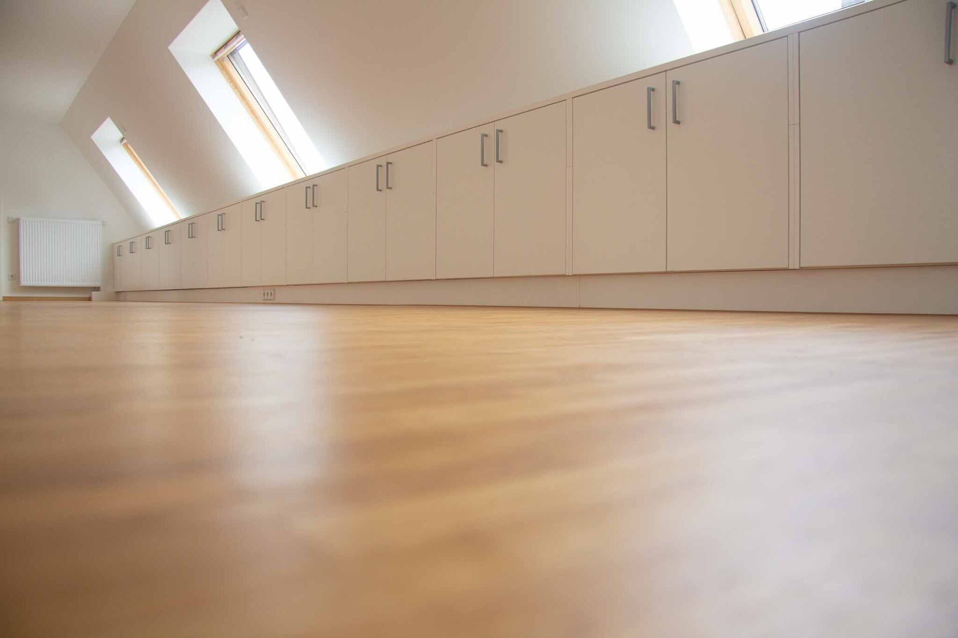 Hartholzboden mit langen weißen Schränken unter schrägen Fenstern.