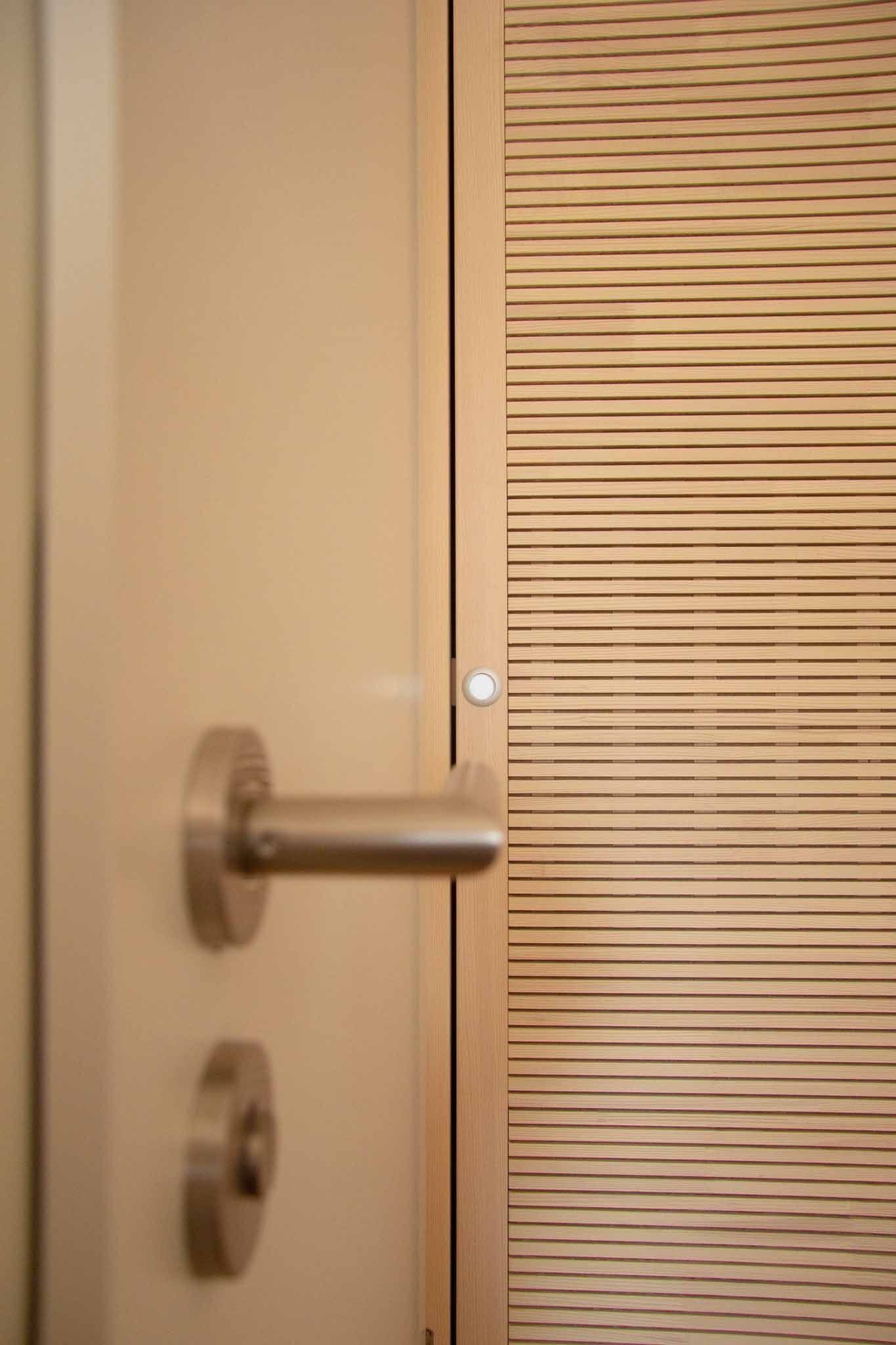 Hellbeige Tür mit horizontaler Holzlamellenplatte und silbernem Griff.