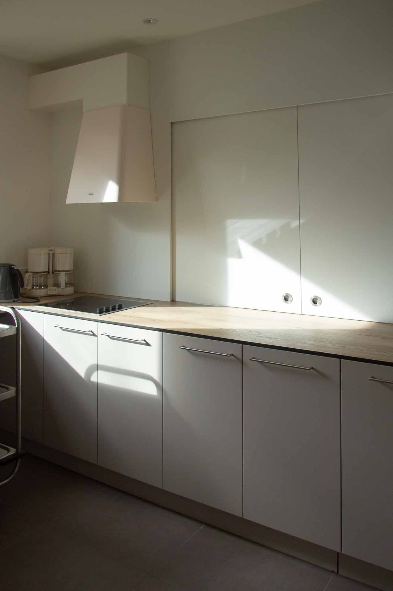 Küche mit weißen Schränken, Holzarbeitsplatte und Sonnenlicht, das den Raum erhellt.