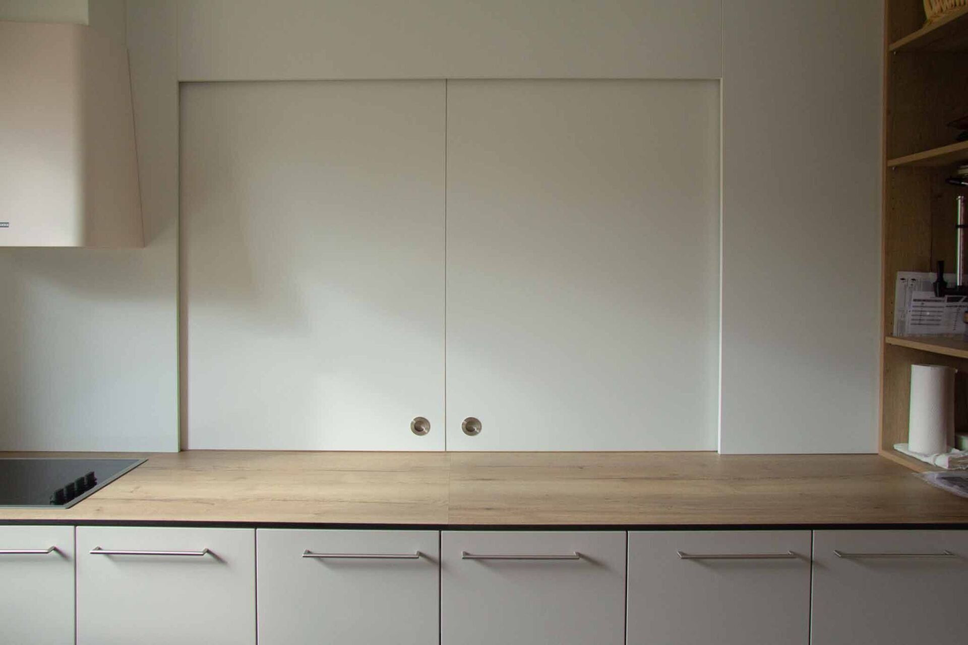 Weiße Küchenschränke und Arbeitsplatte mit zwei eingebauten Schiebetüren mittig über der Arbeitsplatte.