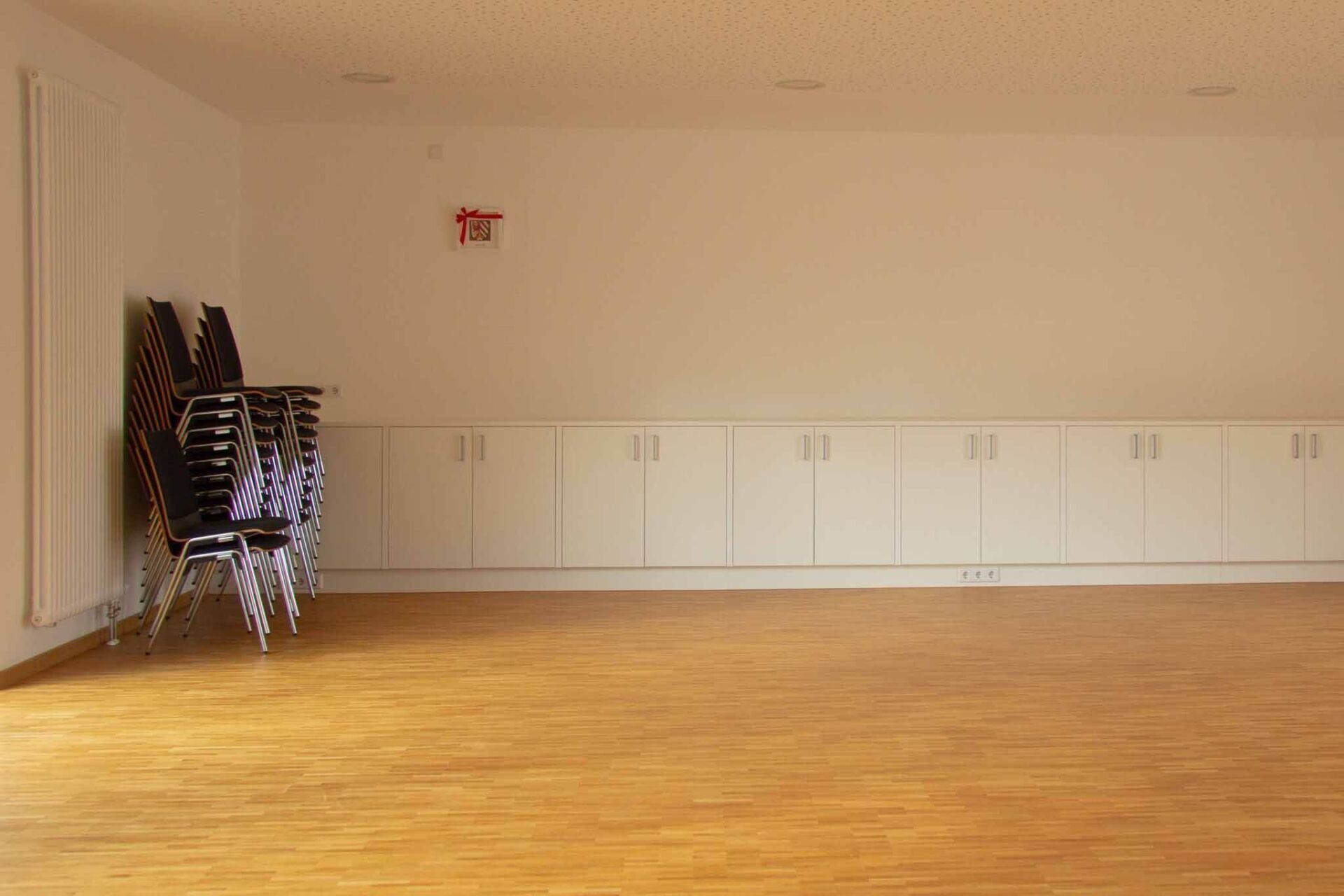 Leerer Raum mit gestapelten Stühlen, Einbauschränken und Holzboden. Beige Wände und Decke.